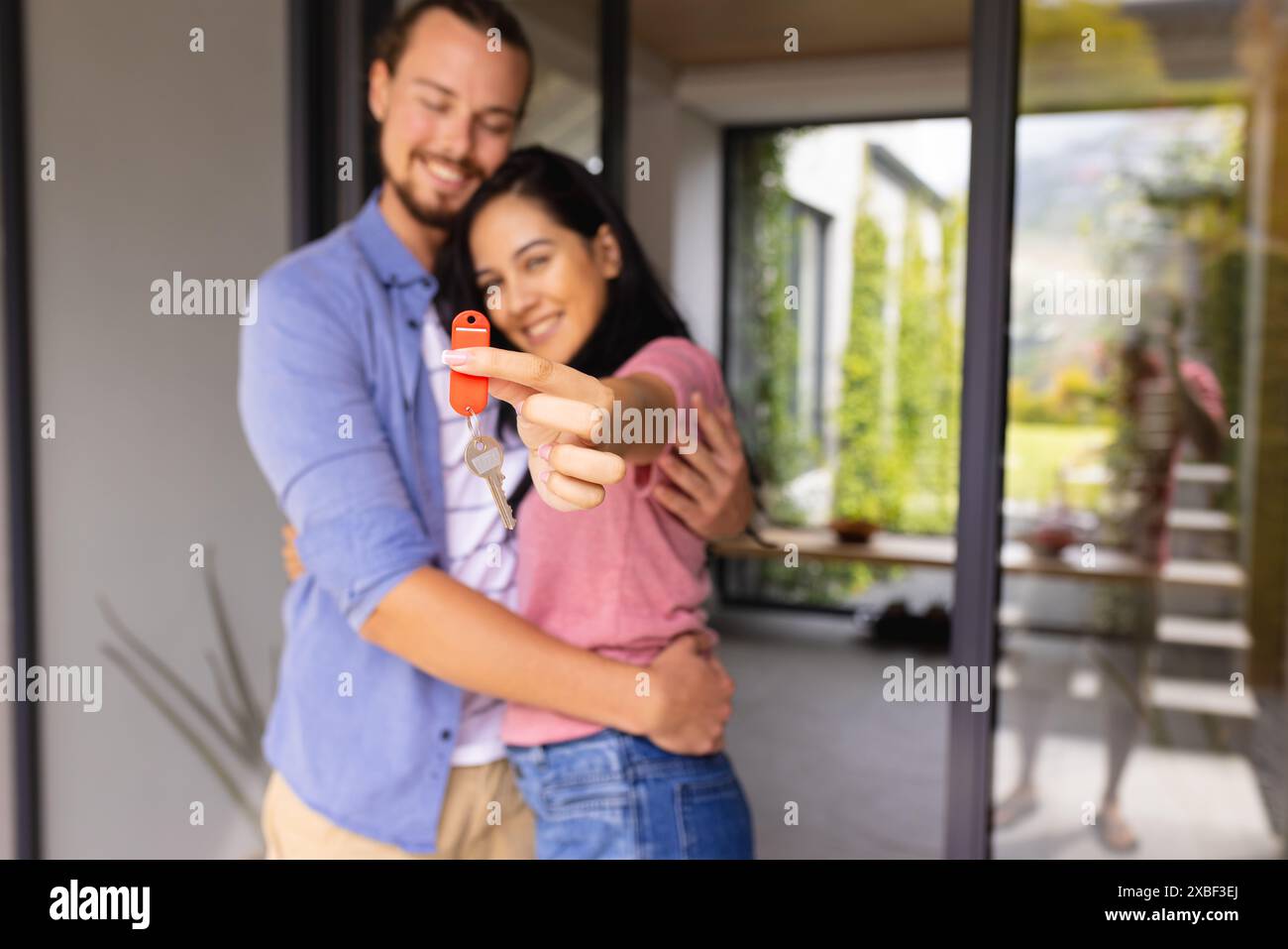 Jeune couple diversifié détiennent les clés de la maison et sourient, achetant la première maison. Ils se tiennent devant une maison moderne avec de grandes fenêtres et plus verte Banque D'Images Jeune couple diversifié détiennent les clés de la maison et sourient, achetant la première maison. Ils se tiennent devant une maison moderne avec de grandes fenêtres et plus verte Banque D'Images