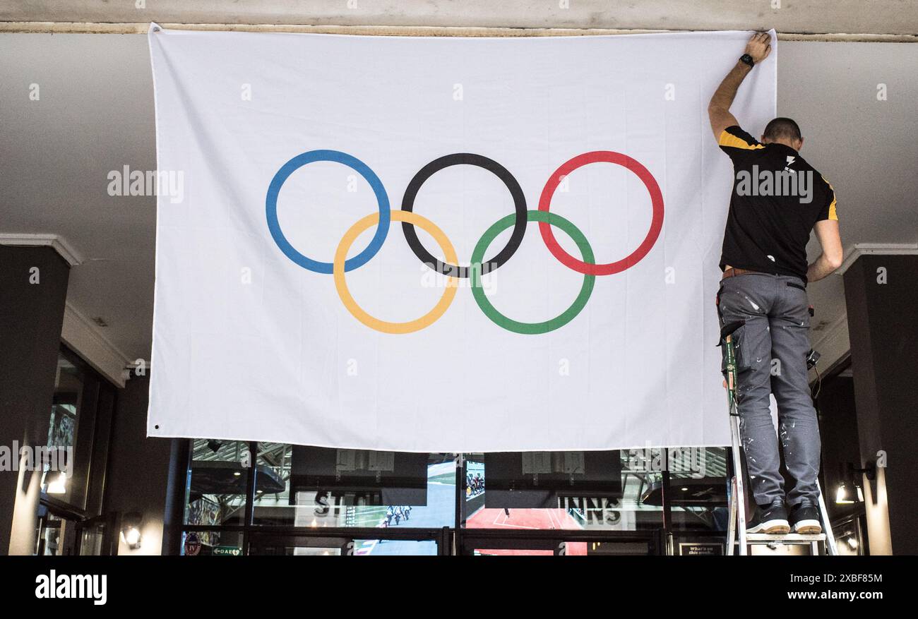 JEUX OLYMPIQUES DE PARIS 2024 - HOMME ACCROCHANT LE DRAPEAU OLYMPIQUE DANS UN MAGASIN - PRÉPARER LES JEUX OLYMPIQUES - PARIS FRANCE © PHOTOGRAPHIE : F. BEAUMONT Banque D'Images