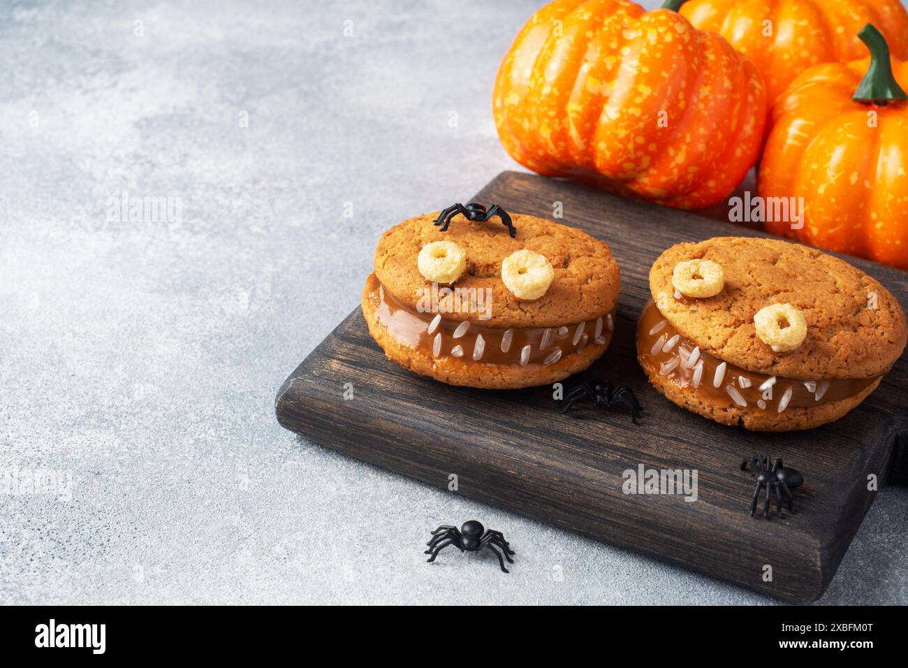 Biscuits avec de la pâte de crème en forme de monstres pour la célébration d'Halloween. Drôles de visages faits maison faits de biscuits à l'avoine et de lait condensé bouilli co Banque D'Images Biscuits avec de la pâte de crème en forme de monstres pour la célébration d'Halloween. Drôles de visages faits maison faits de biscuits à l'avoine et de lait condensé bouilli co Banque D'Images