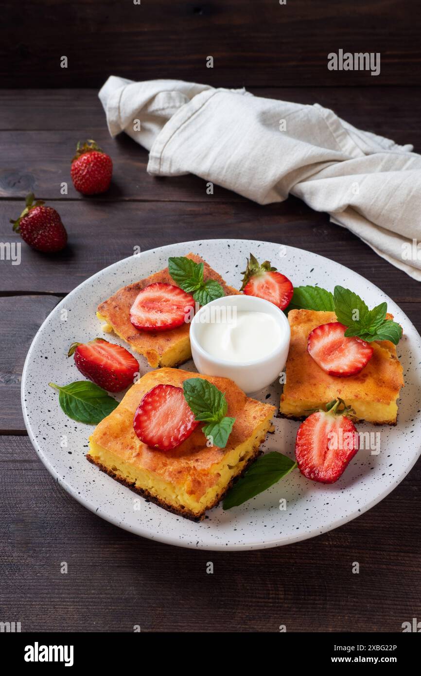 Casserole de fromage cottage avec fraises et menthe. Délicieux dessert fait maison à base de lait caillé et de baies fraîches avec fond en bois foncé crème, copie Banque D'Images Casserole de fromage cottage avec fraises et menthe. Délicieux dessert fait maison à base de lait caillé et de baies fraîches avec fond en bois foncé crème, copie Banque D'Images