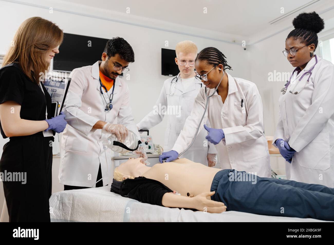 Les étudiants en médecine pratiquent la RCP sur un mannequin. Ils portent des manteaux blancs, des gants ; l'un utilise un masque à valve de sac, l'autre écoute avec un stéthoscope. Banque D'Images