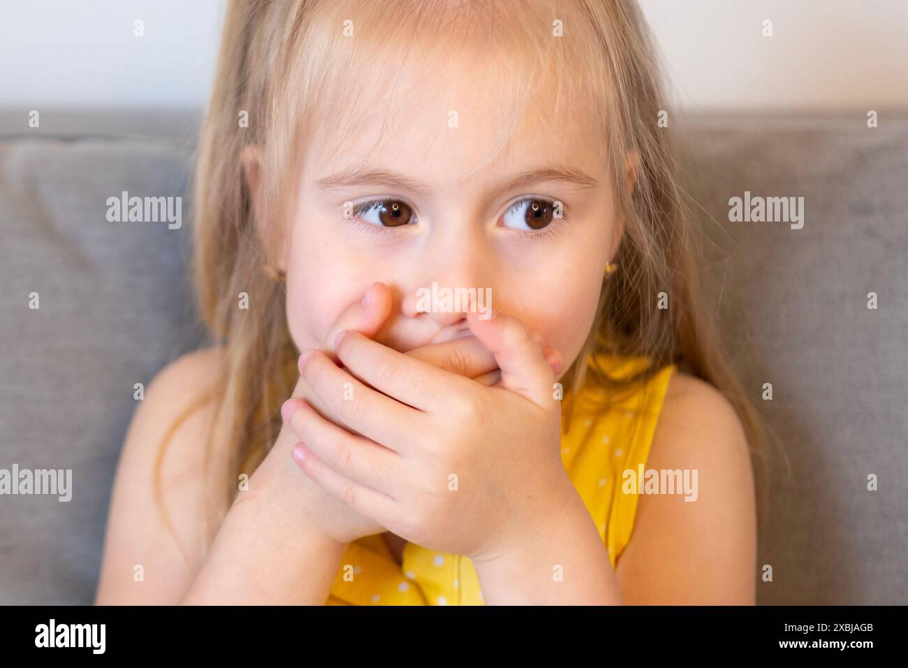 Doux enfant de 5 ans, fille blonde timide couvert la bouche avec les mains, lutte pour garder le secret et maintenir l'autodiscipline, les difficultés de contrôle, l'esprit yo Banque D'Images