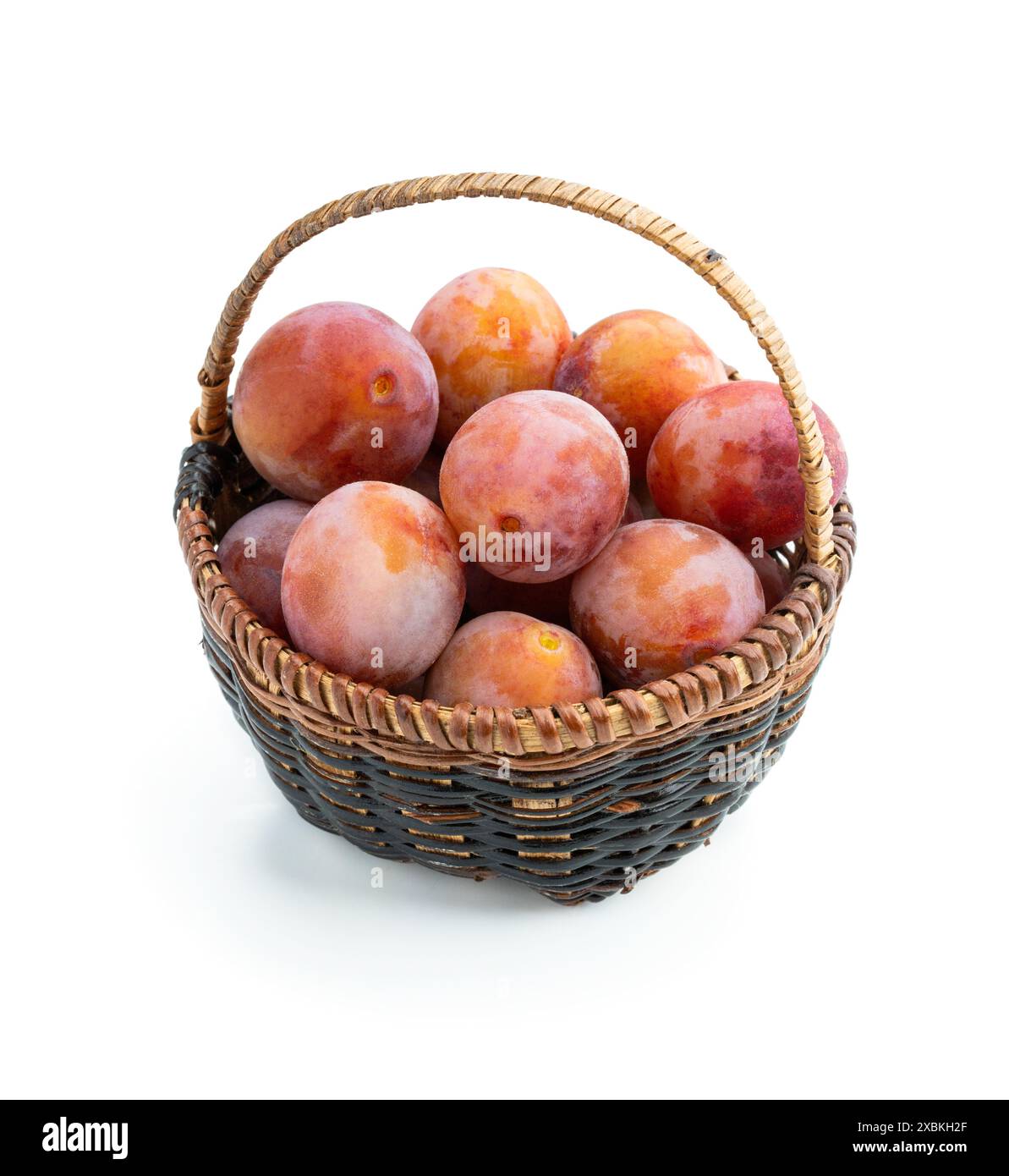 Prunes mûres violettes dans un panier en osier isolé sur fond blanc Banque D'Images