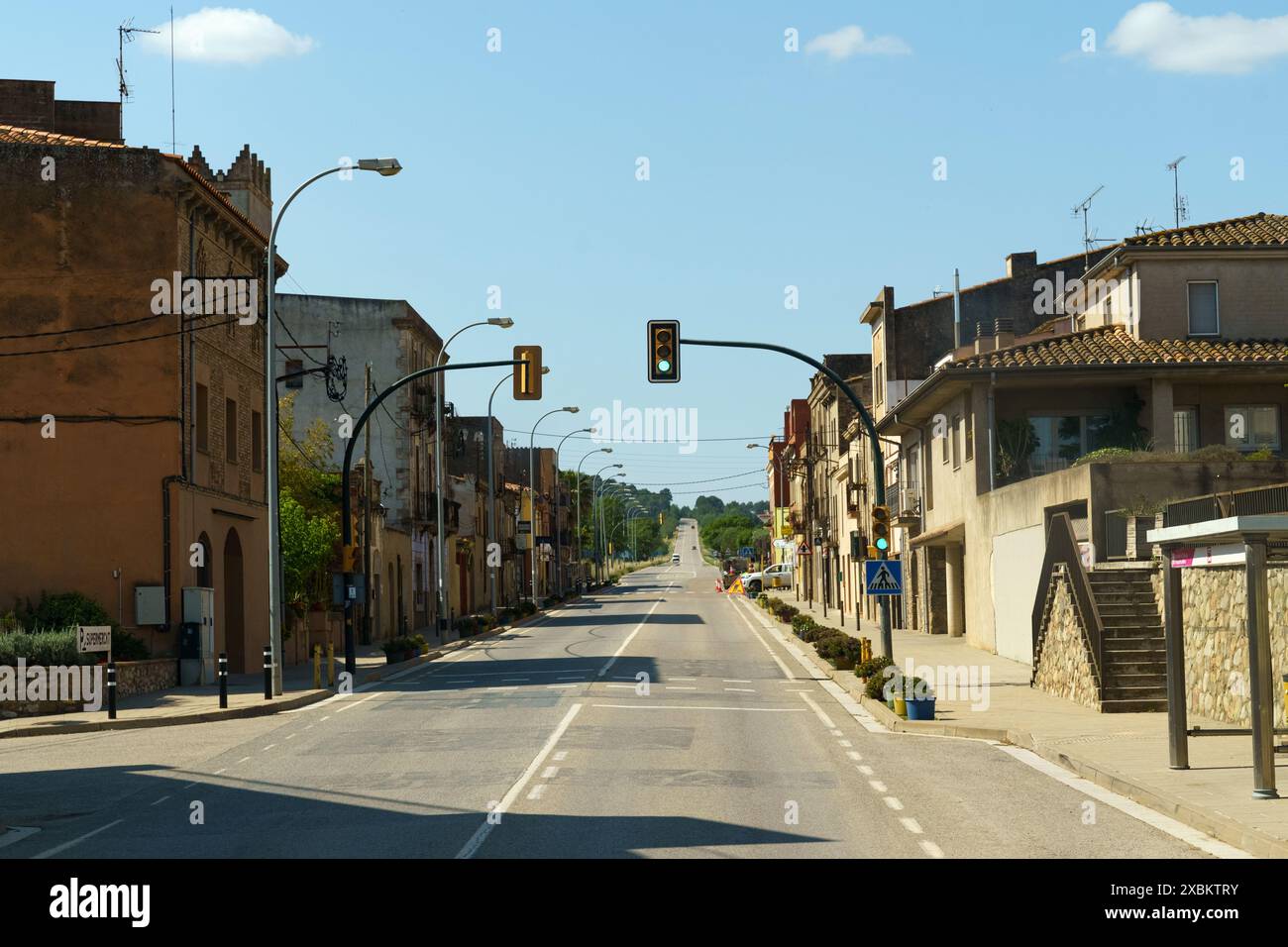 Une rue calme dans une ville espagnole, avec des bâtiments bordant les deux côtés et un feu de circulation au bout de la route. Le soleil brille. Banque D'Images