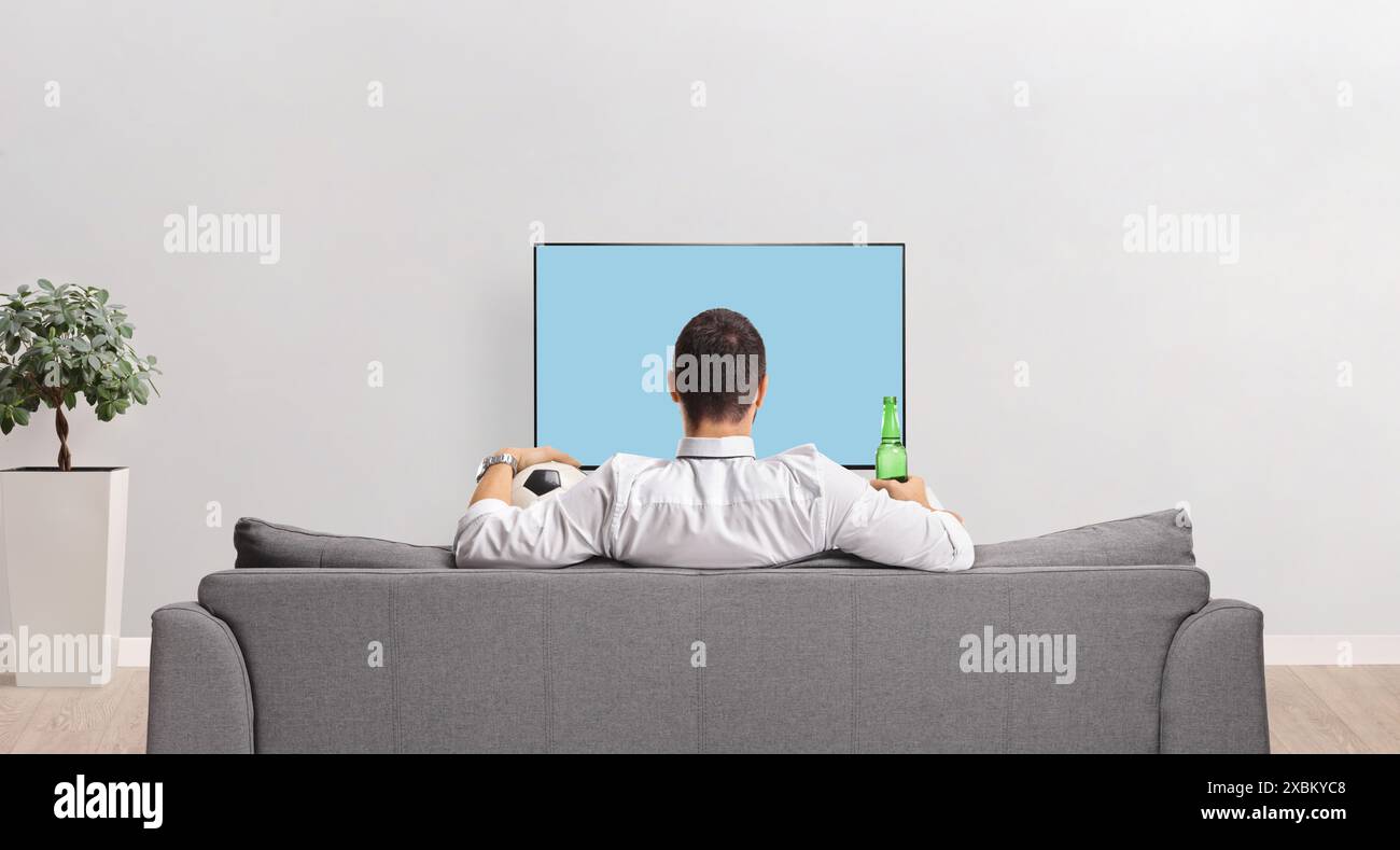 Vue arrière d'un homme devant la télévision avec une bouteille de bière et un ballon de football à la maison Banque D'Images