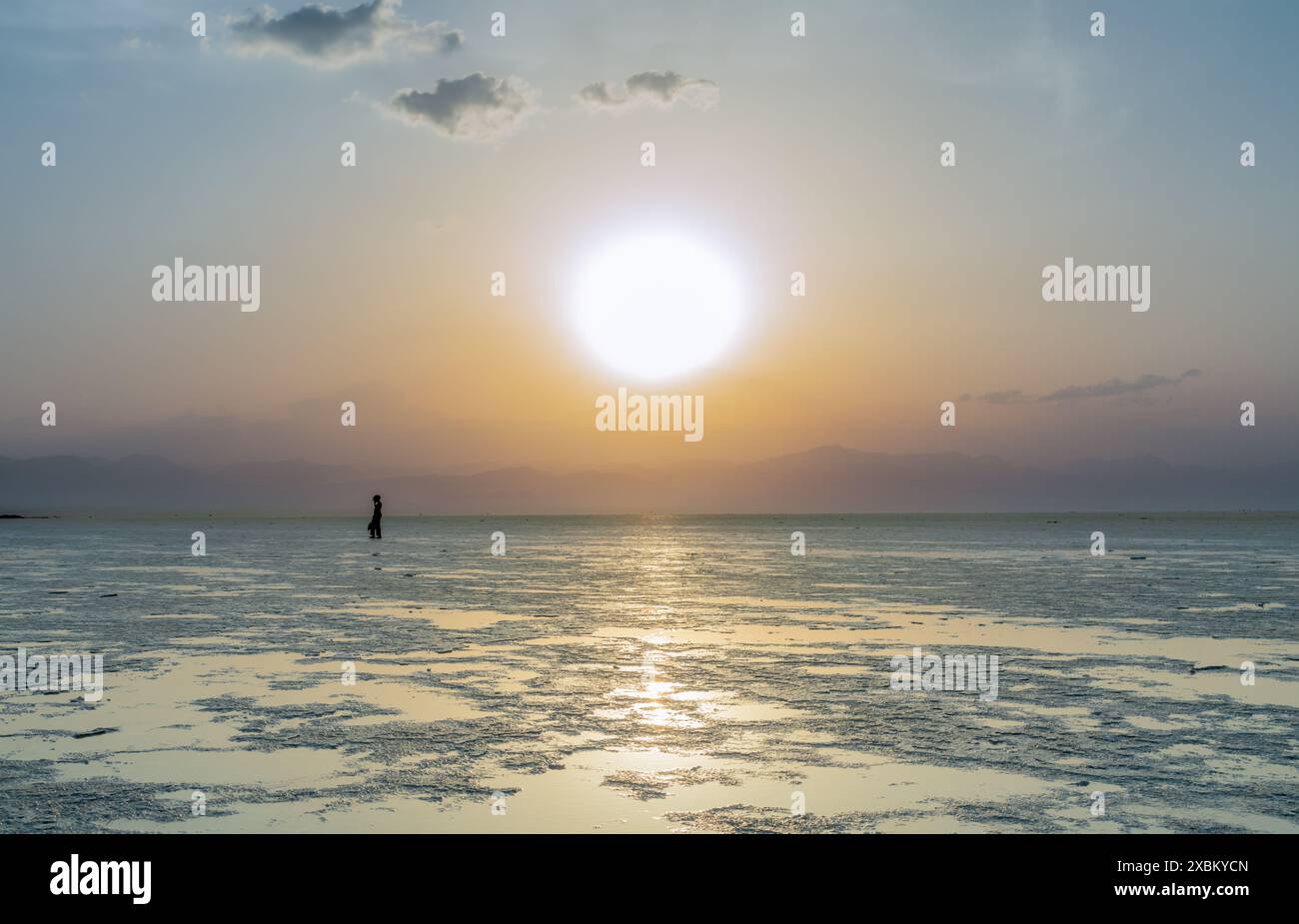 Les femmes figurent dans un coucher de soleil sur la surface du lac de sel blanc Karum, désert de dépression Danakil, région d'Afar, Ethiopie Banque D'Images