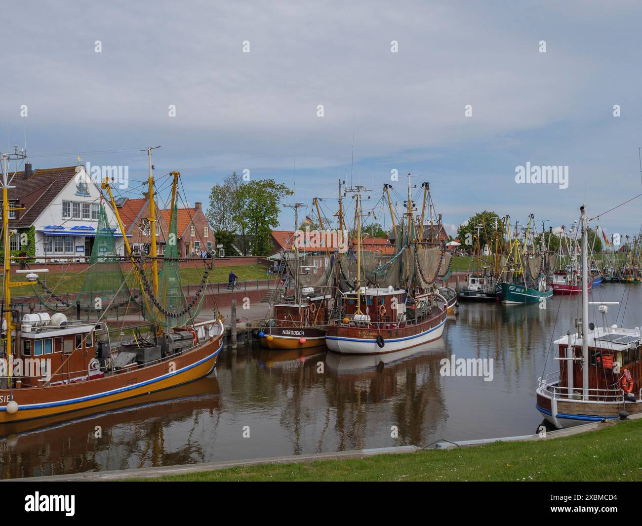 Une rangée de bateaux de pêche se trouve dans le port en face d'un village par beau temps d'été, Greetsiel, Frise orientale, basse-Saxe, Allemagne Banque D'Images