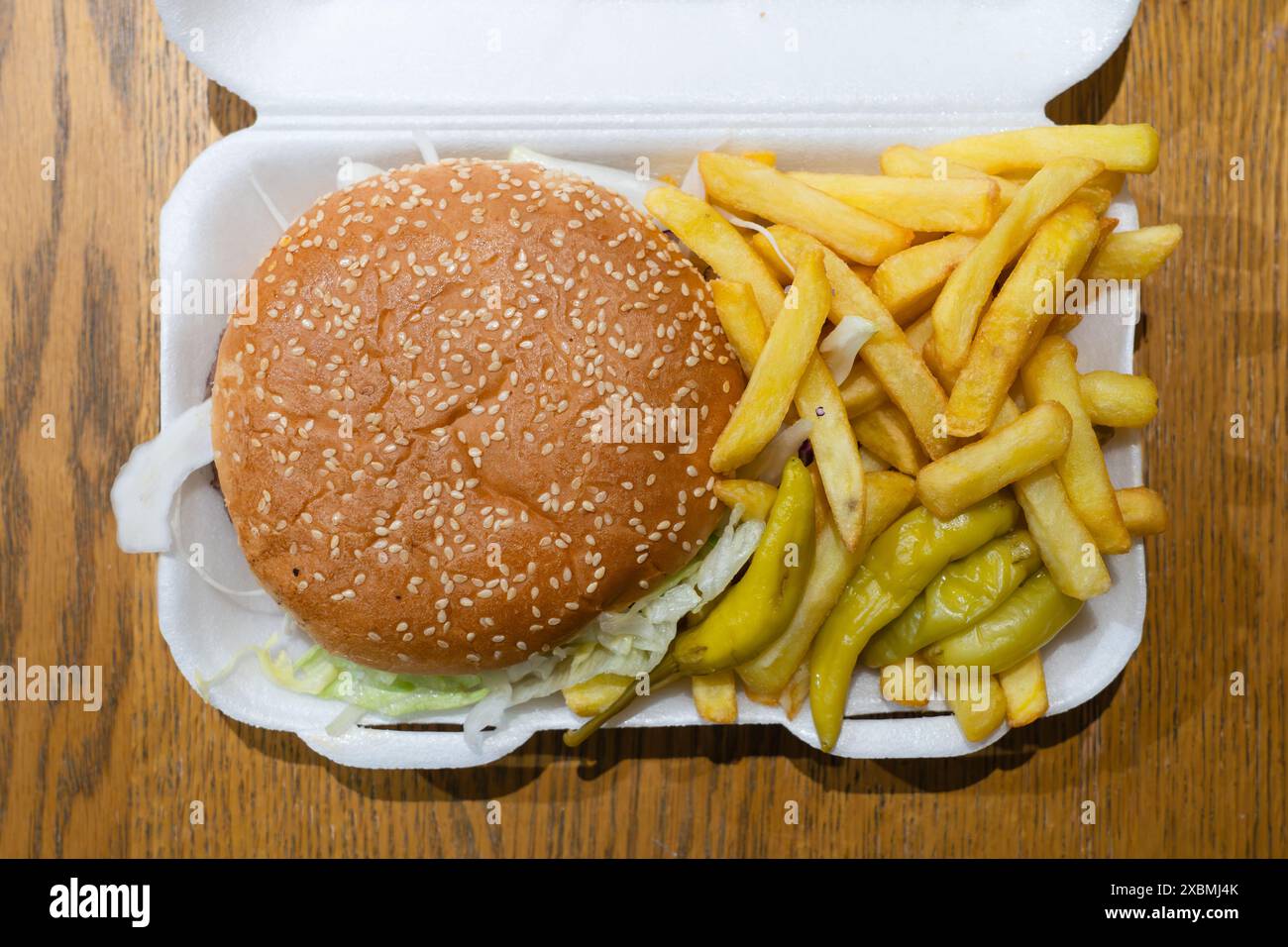 Un cheeseburger à emporter et des chips avec des poivrons jalapeno dans un carton de polystyrène à la maison, au Royaume-Uni. Concept : aliments gras, restauration rapide, plats à emporter, crise d'obésité Banque D'Images