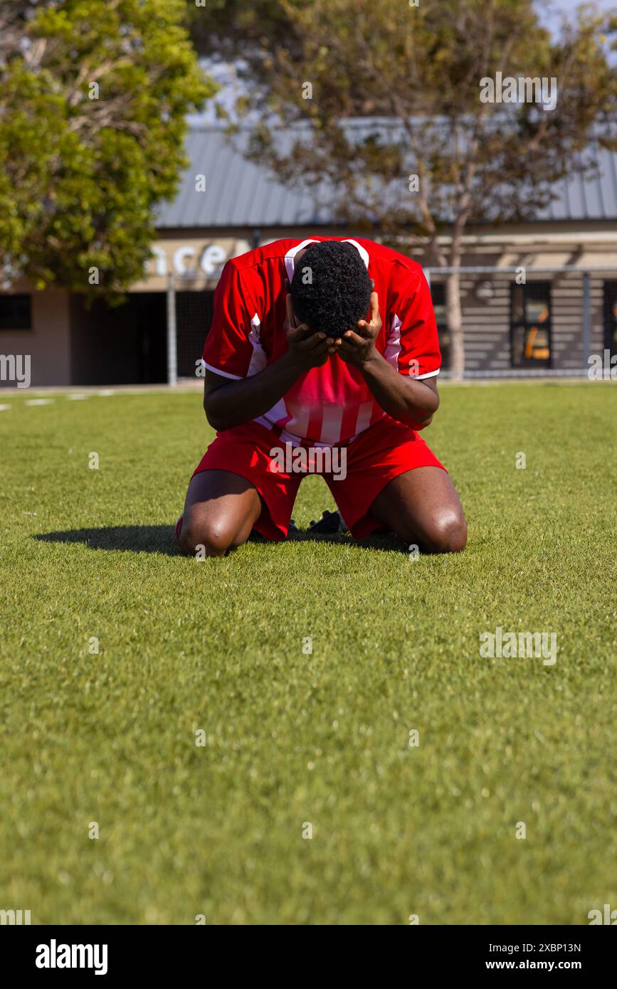 Joueur de football afro-américain agenouillé sur un terrain d'herbe, apparaissant émotionnel, espace de copie Banque D'Images