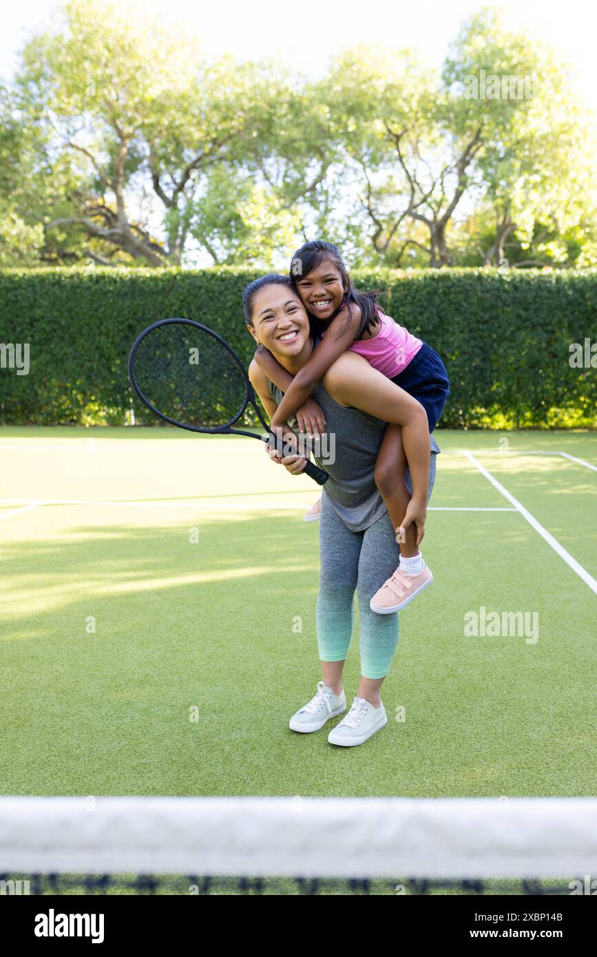 Portrait de mère biraciale donnant cochon en retour à sa fille sur un court de tennis Banque D'Images