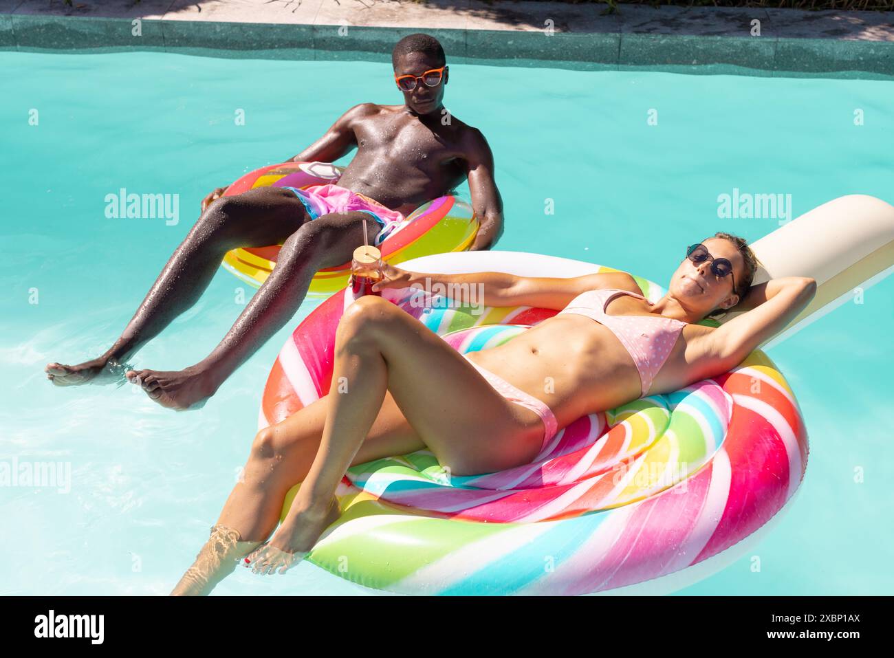 Un couple diversifié se relaxant sur les flotteurs colorés de piscine par piscine, soleil d'été bonheur amour Banque D'Images