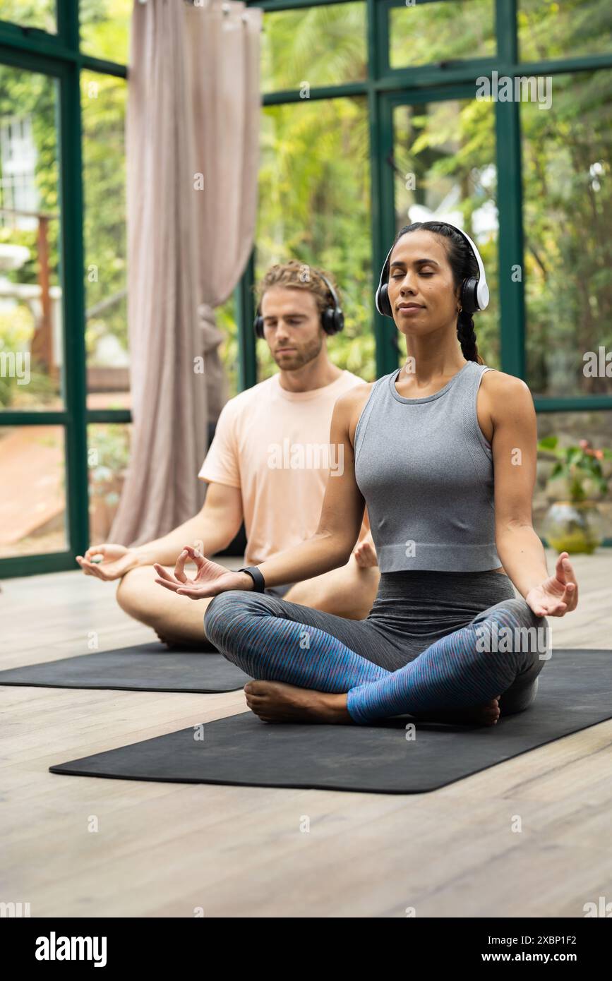 Une femme biraciale et un homme caucasien méditant avec des écouteurs en cours de yoga Banque D'Images