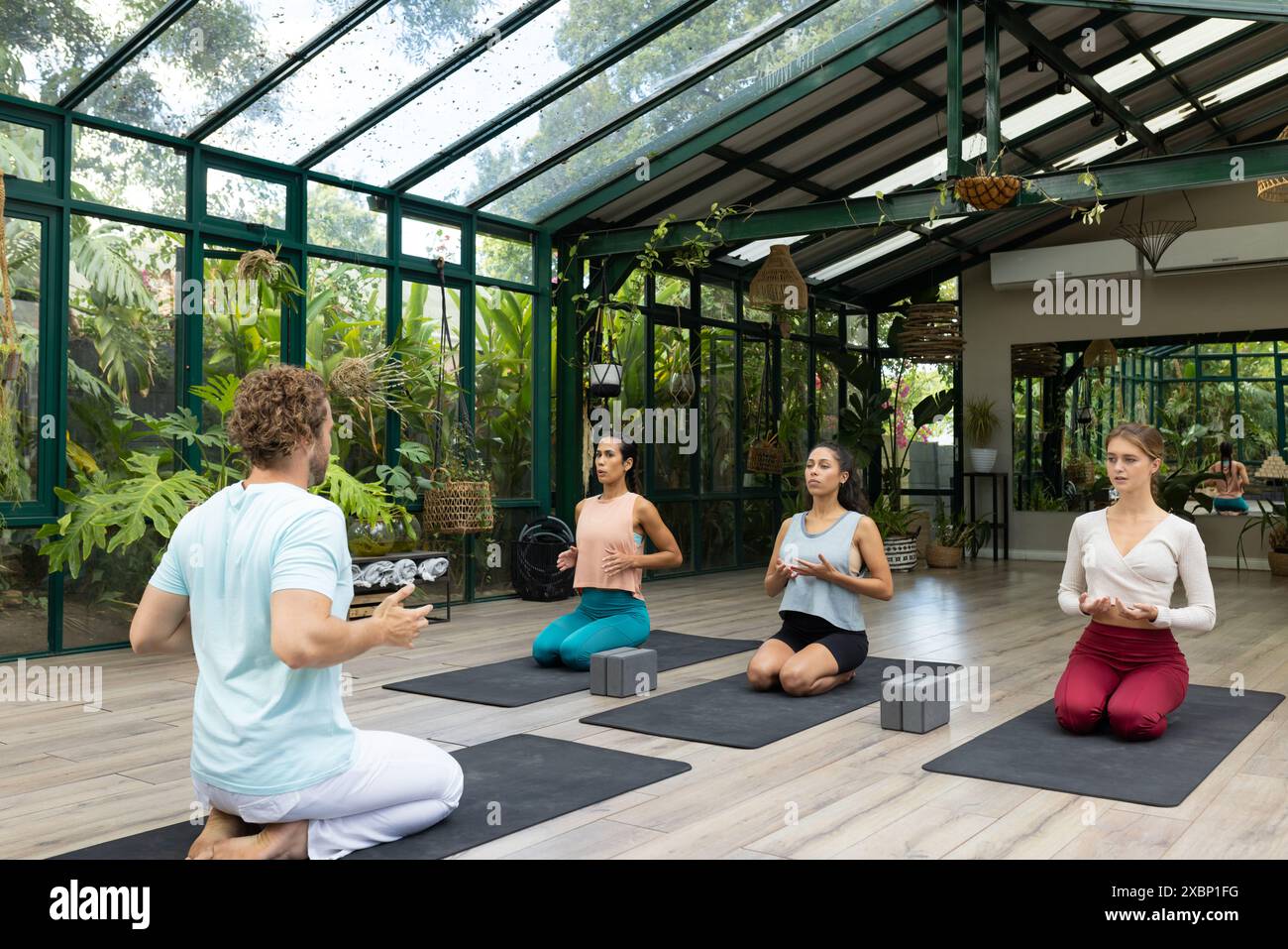 Groupe diversifié de personnes à la classe de yoga méditant dans le studio de maison de verre Banque D'Images