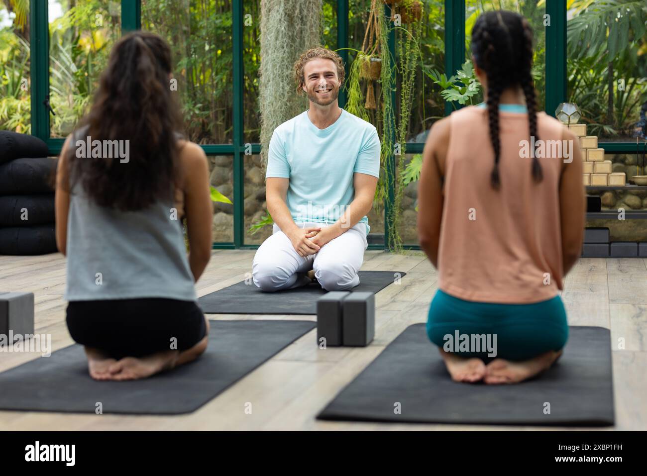 Un groupe diversifié de personnes au cours de yoga est assis sur des tapis dans une maison de verre sereine Banque D'Images