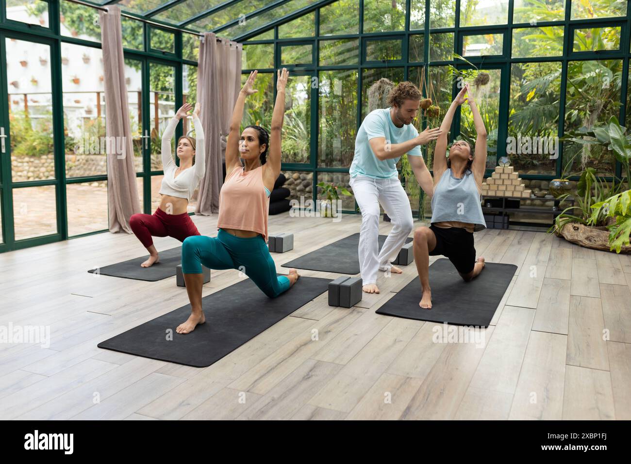 Un groupe diversifié de personnes au cours de yoga et des instructeurs pratiquent le yoga dans une maison de verre Banque D'Images