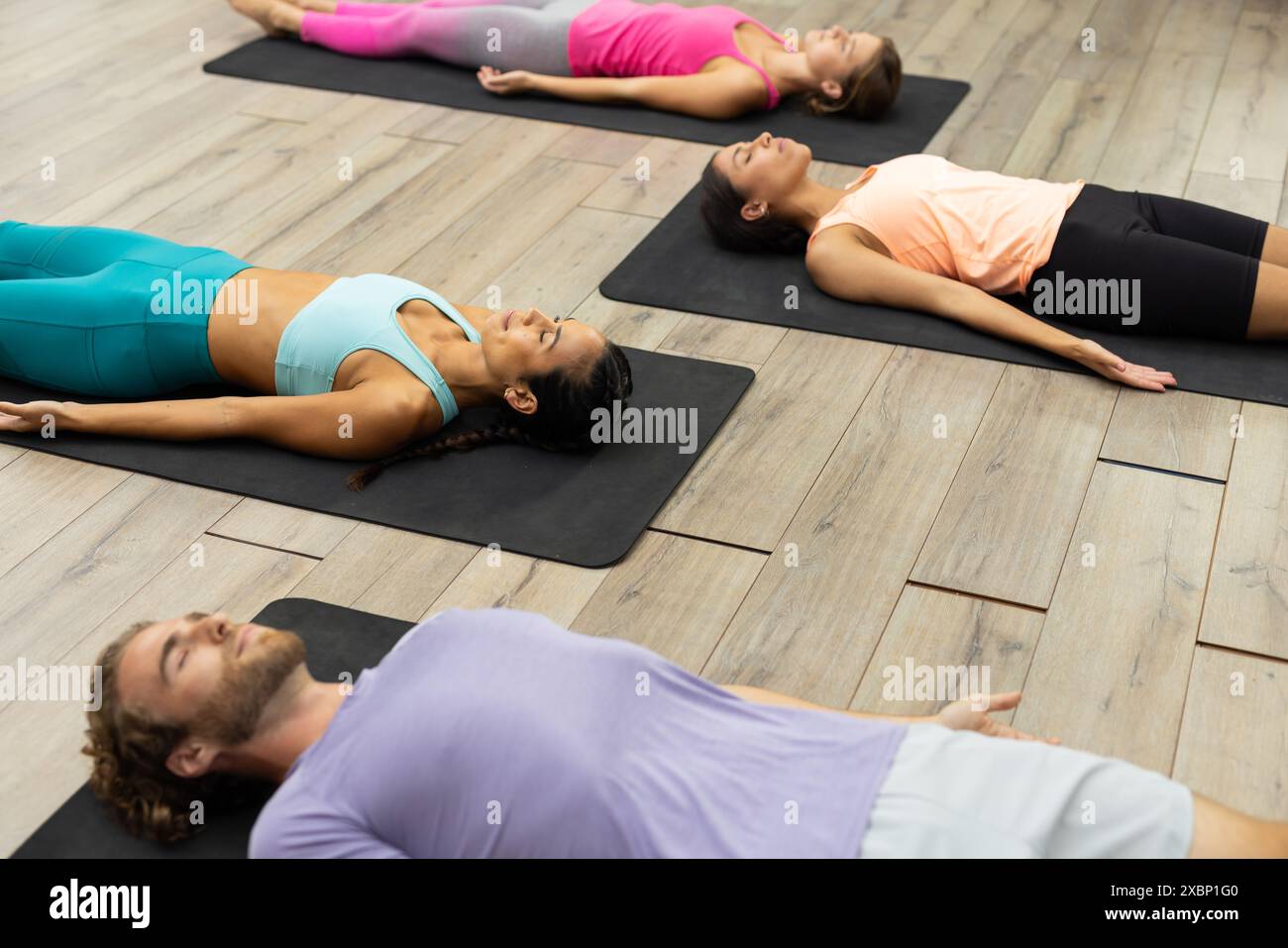 Un groupe diversifié de personnes au cours de yoga est allongé sur des tapis dans le studio de yoga serein Banque D'Images
