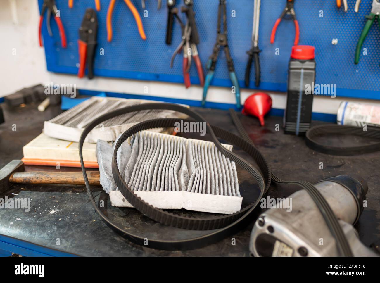 Par dessus le filtre à air endommagé et la courroie d'entraînement placé sur le bureau de réparation mécanicien près de divers outils sur le mur avec la bouteille d'huile pendant le travail dans le garage Banque D'Images