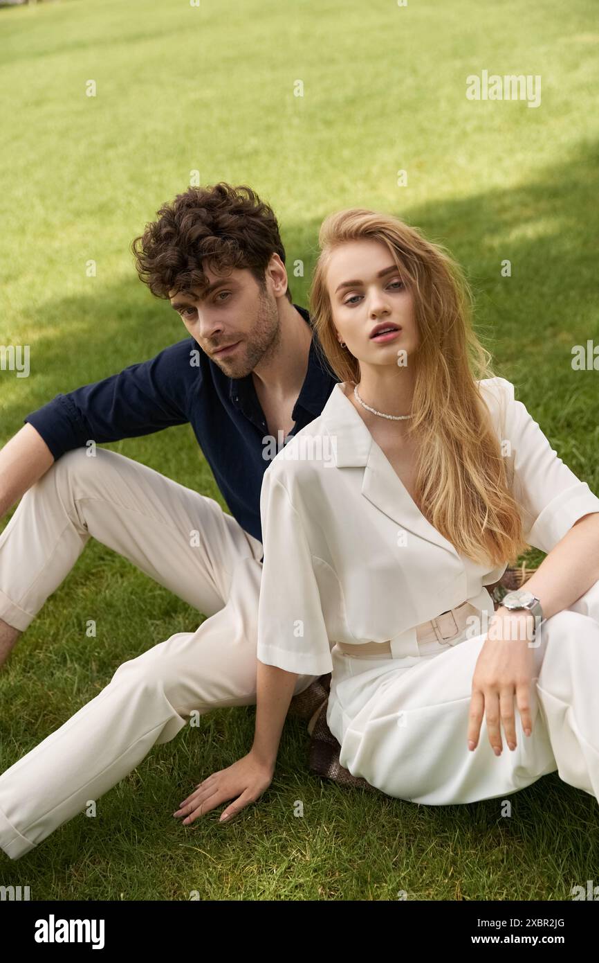 Jeune couple dans une tenue élégante se relaxant sur l'herbe, incarnant le vieux style de l'argent au milieu d'un champ vert luxuriant. Banque D'Images