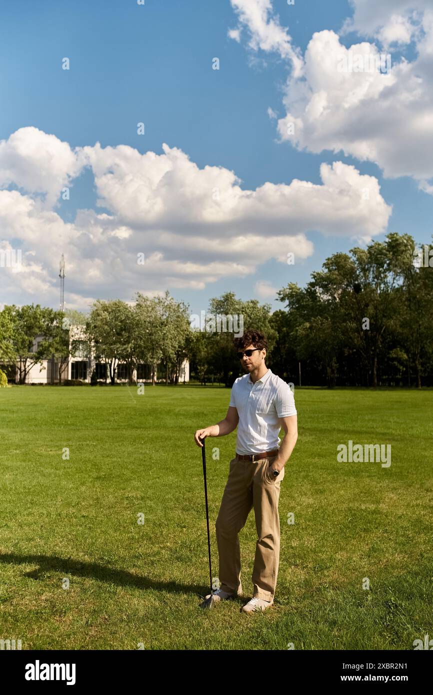 Un homme élégant se tient dans un champ verdoyant, saisissant un club de golf, entouré de natures de beauté paisible. Banque D'Images