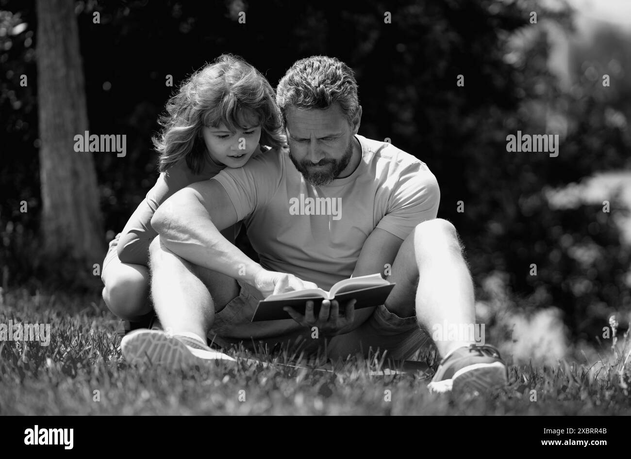 Père et fils lisant un livre dans le parc. Le concept d'éducation et d'amitié. Style de vie, père a lu un livre à son fils mignon en plein air, été chaud Banque D'Images