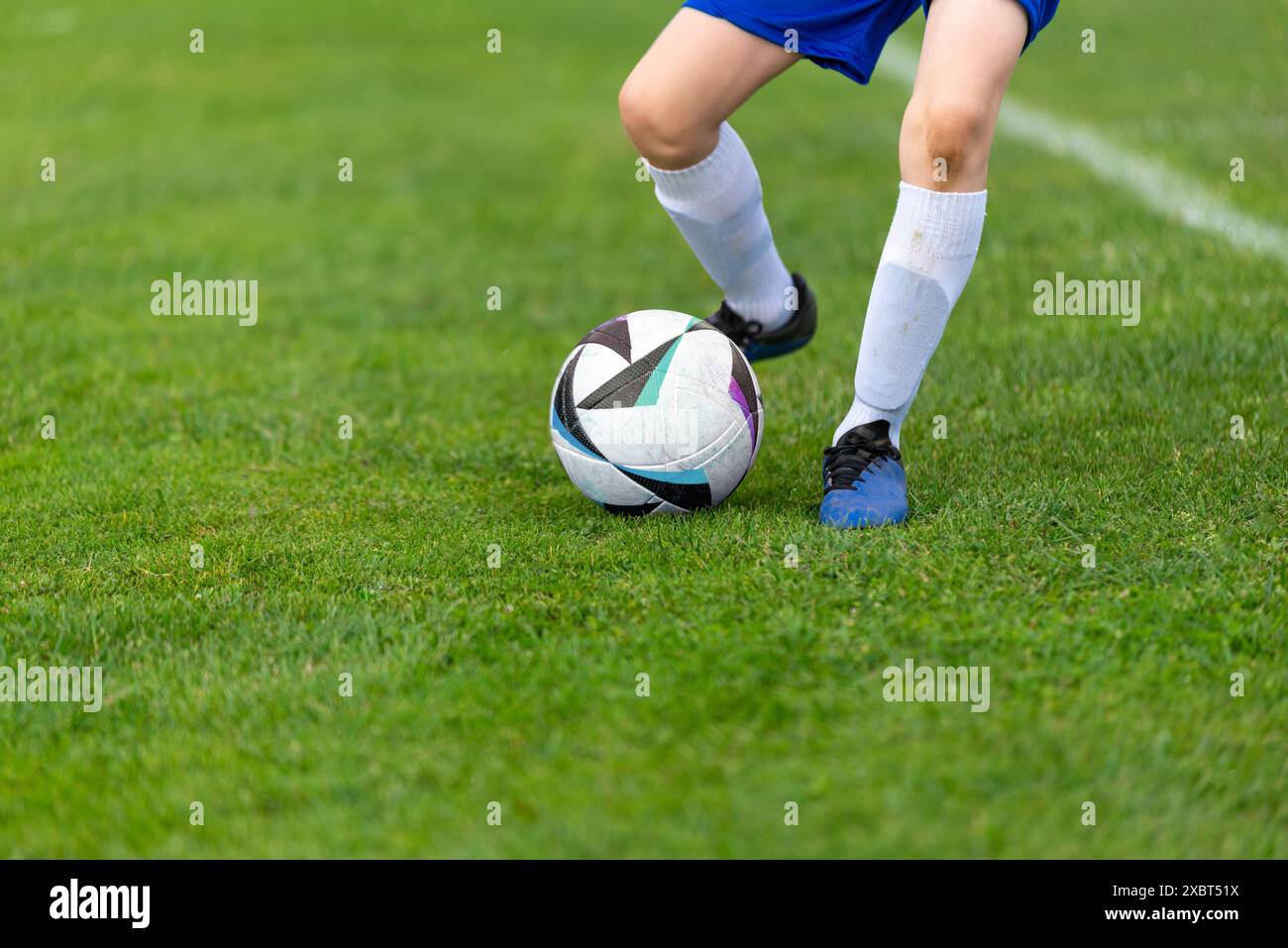 Ballon de coup de pied d'un jeune footballeur. Balle et jambes nettes sur un terrain vert luxuriant gros plan Banque D'Images