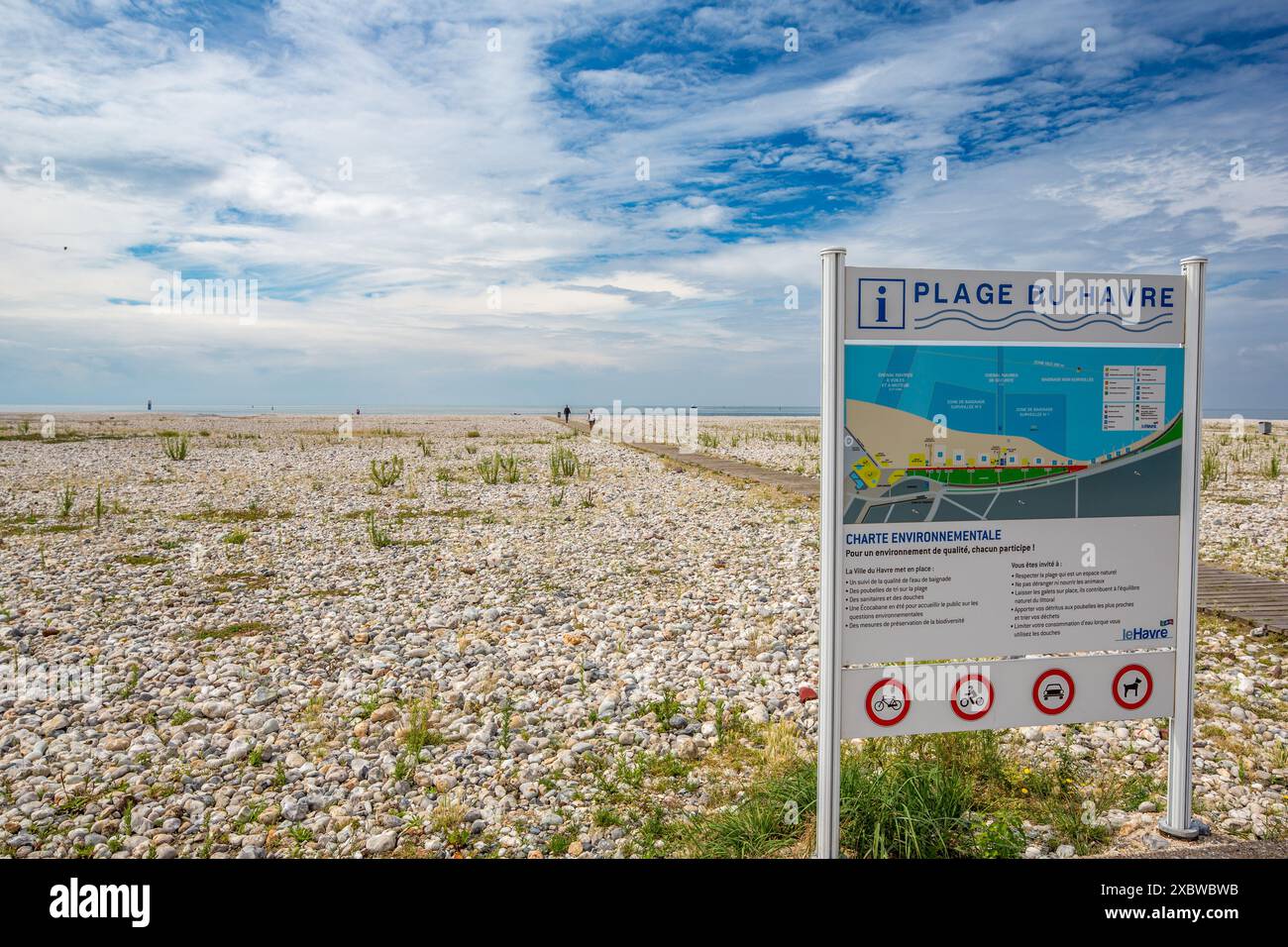 Vue grand angle de la plage rocheuse plage du Havre au Havre, France, avec un panneau clair avec des directives de plage et un ciel partiellement nuageux. Banque D'Images