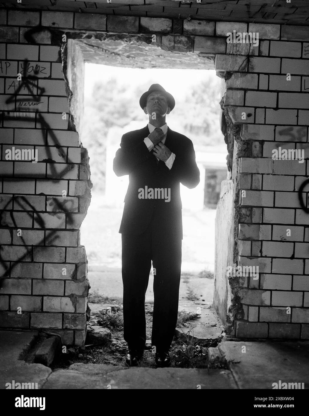 Homme mi-adulte en costume et chapeau ajustant la cravate tout en se tenant debout dans la porte ouverte Banque D'Images