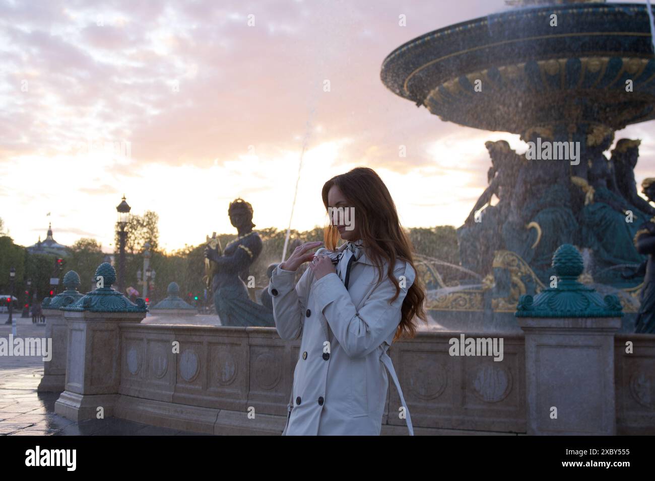 Belle fille se tient près d'une fontaine au coucher du soleil sur une place à Paris au printemps Banque D'Images