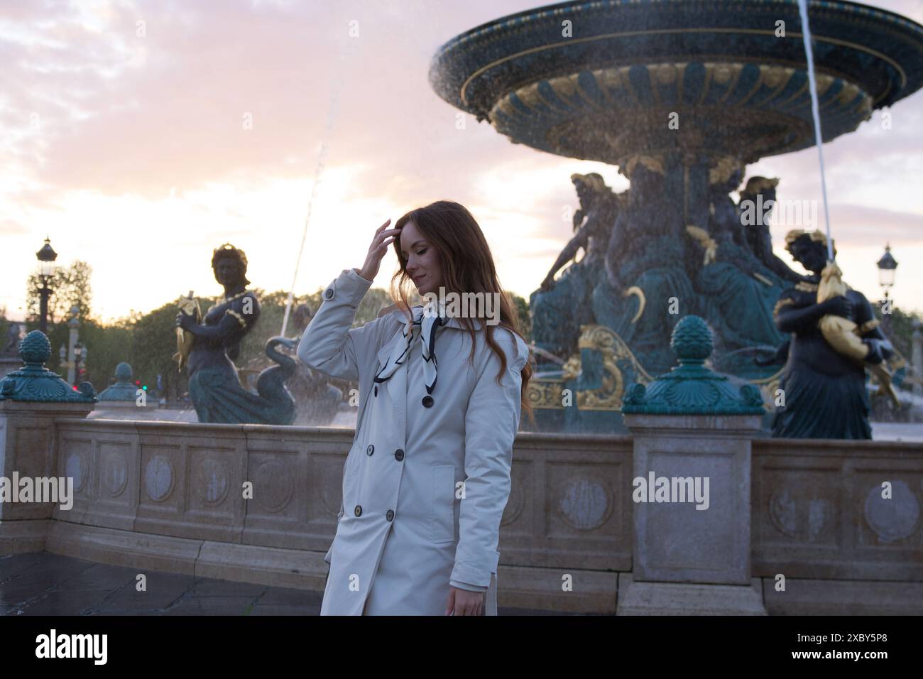 Belle fille se tient près d'une fontaine au coucher du soleil sur une place à Paris au printemps Banque D'Images