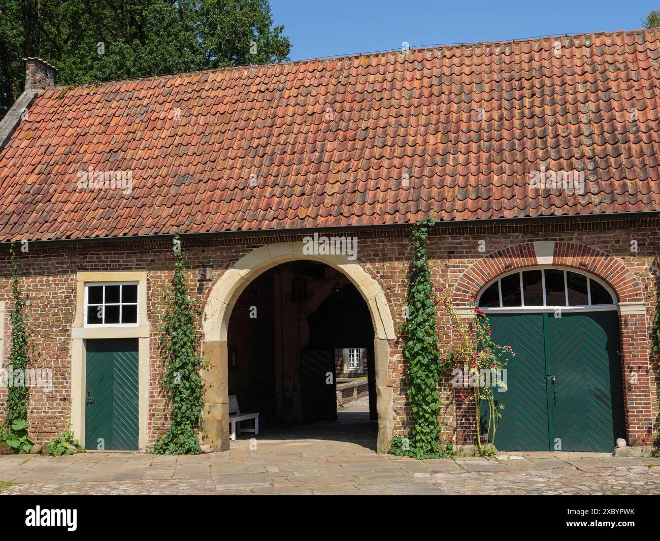 Une maison en brique avec une arche ronde, tuiles rouges sur le toit, portes vertes et entourée de plantes grimpantes, ochtrup, muensterland, allemagne Banque D'Images