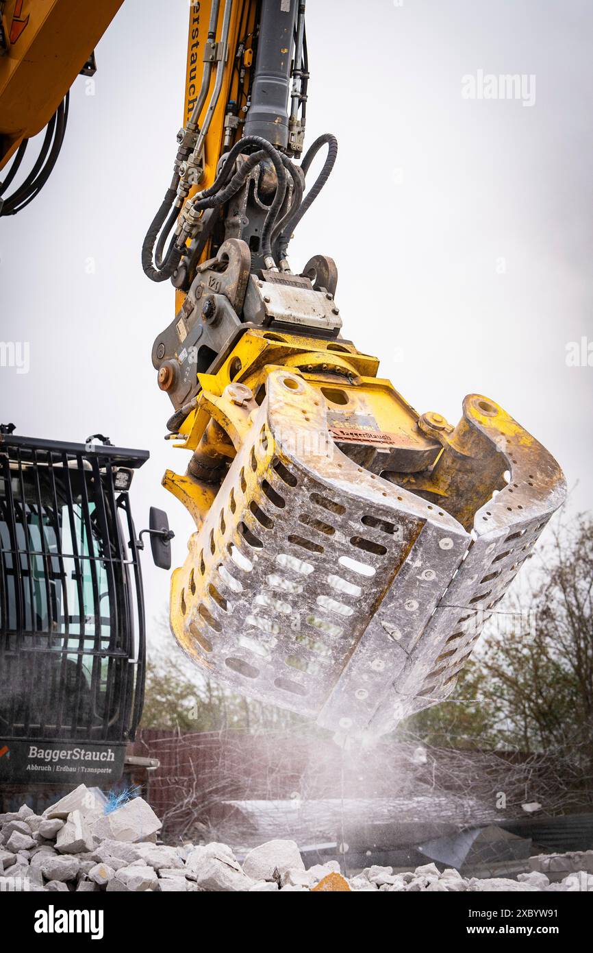 Excavatrice jaune avec une pince métallique massive nettoie les débris sur un chantier de construction, les éclaboussures d'eau, site de démolition, Saarbruecken, Allemagne Banque D'Images