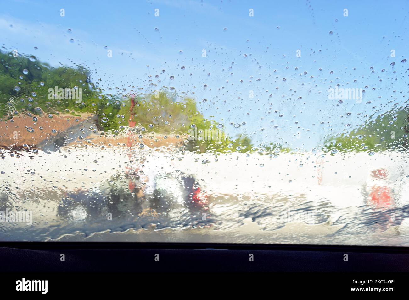 Vue de la rue à travers un pare-brise de voiture recouvert de gouttes d'eau. Photo de l'intérieur d'un véhicule dans un lave-auto. Banque D'Images