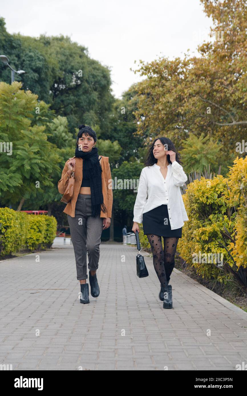 Deux femmes latines marchant dans un parc, elles ont quitté l'université et rentrent chez elles, image verticale, image verticale, elles se divertissent en regardant th Banque D'Images