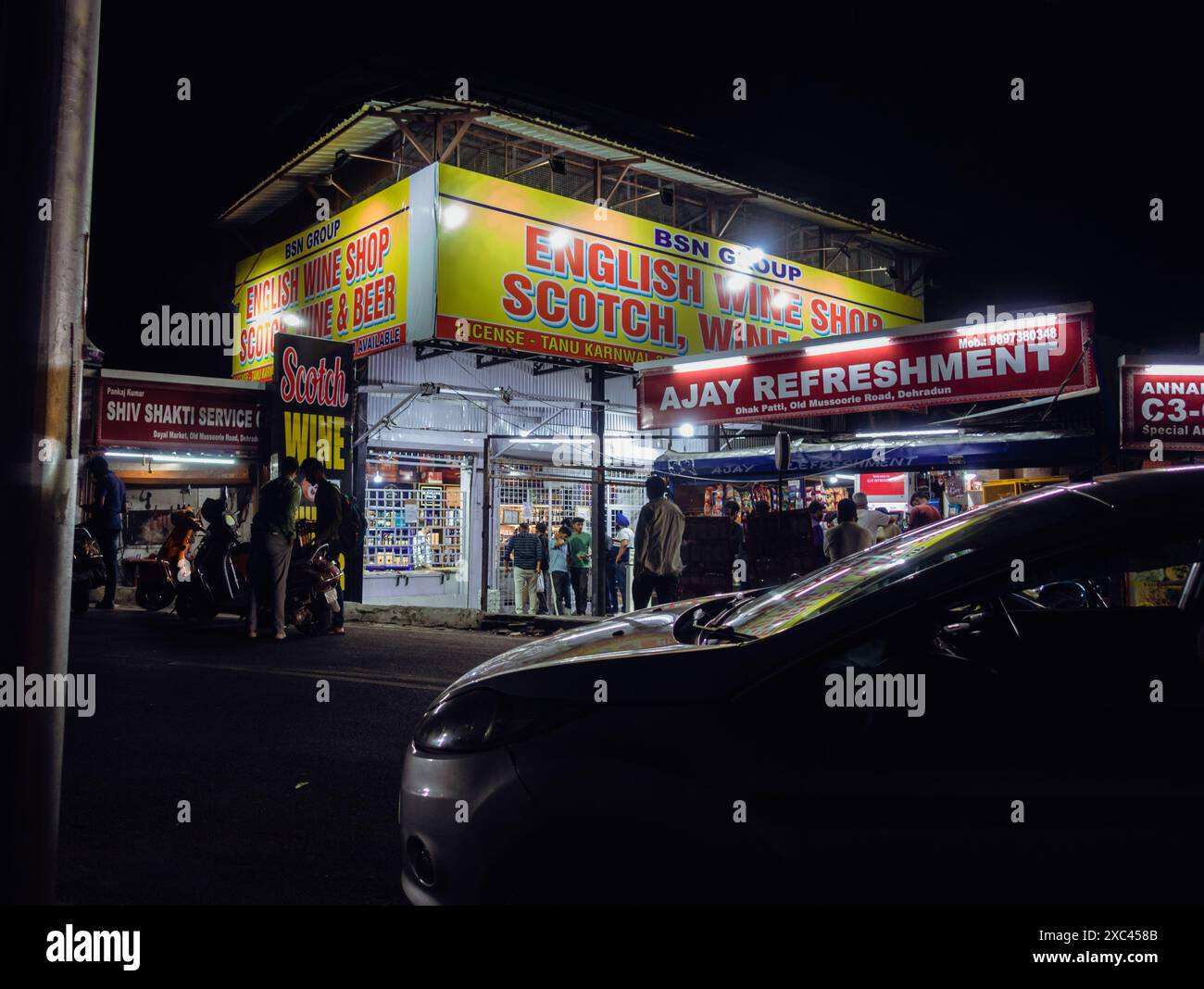 10 juin 2024, Dehradun City Uttarakhand Inde. Magasin d'alcool brillant à Dehradun City, Uttarakhand, Inde, avec des gens faisant la queue la nuit pour acheter de l'alcool Banque D'Images