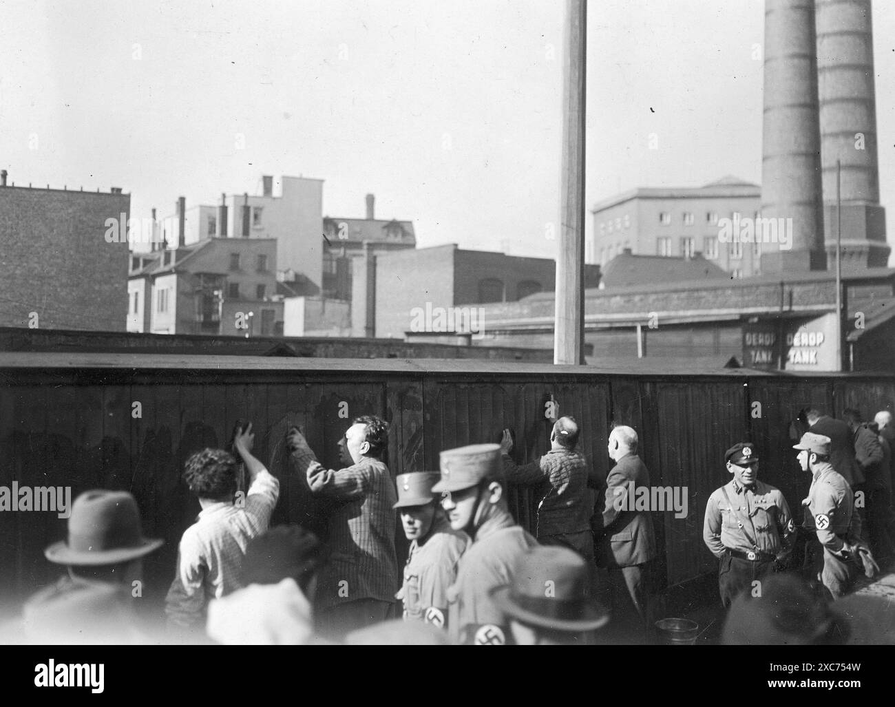 Photo de propagande nazie montrant des Juifs forcés de gratter des affiches de propagande socialiste d'une clôture ou d'un mur entourant une usine, à Berlin vers avril 1933. Ils sont surveillés par des membres en uniforme de la sa (Sturmabteilung), les troupes paramilitaires du parti nazi. Banque D'Images