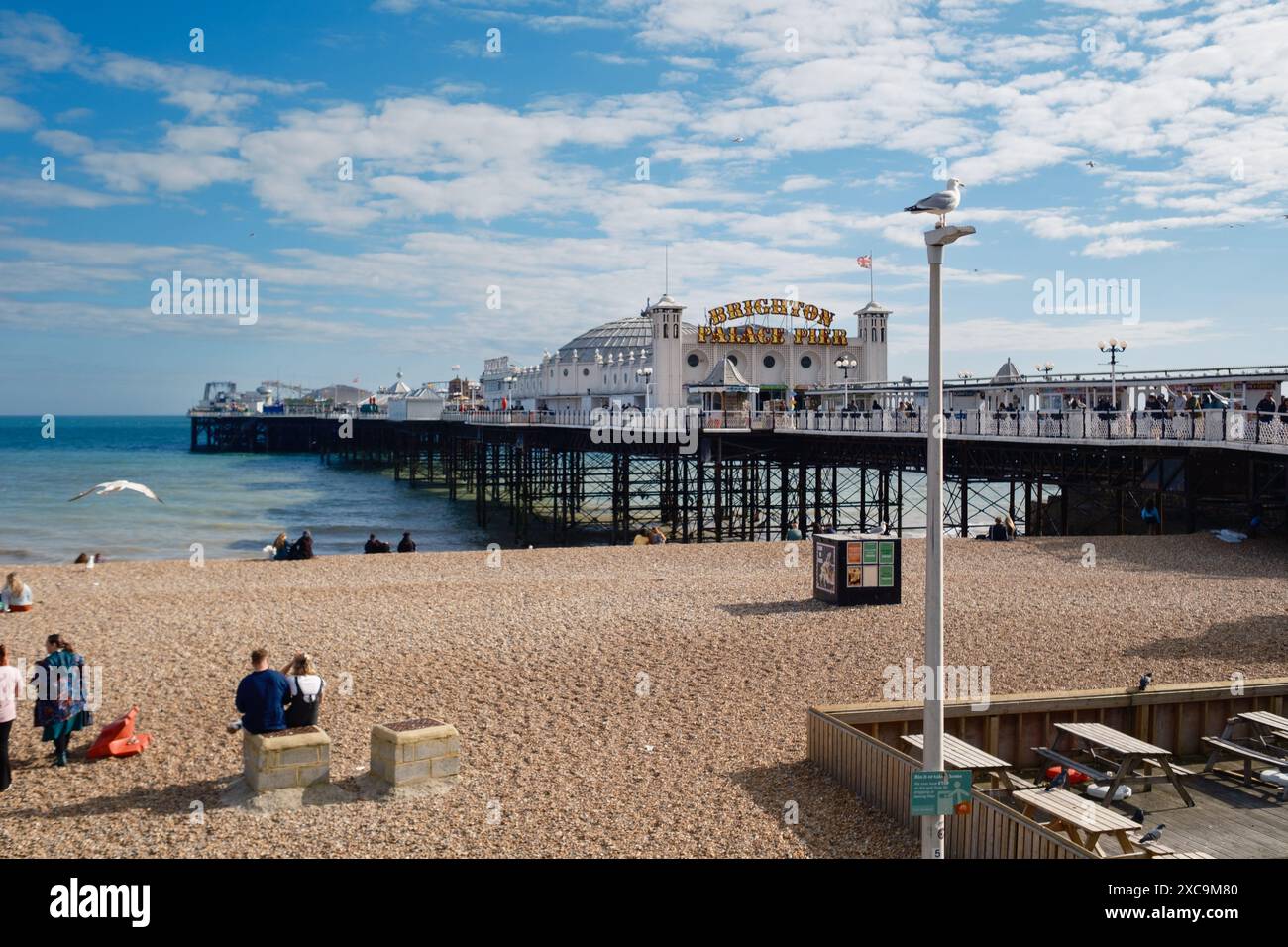 Brighton Palace Pier et une vue sur la plage tranquille par une froide journée d'été avec mouette perchée sur un lampadaire et une dispersion de gens assis Banque D'Images