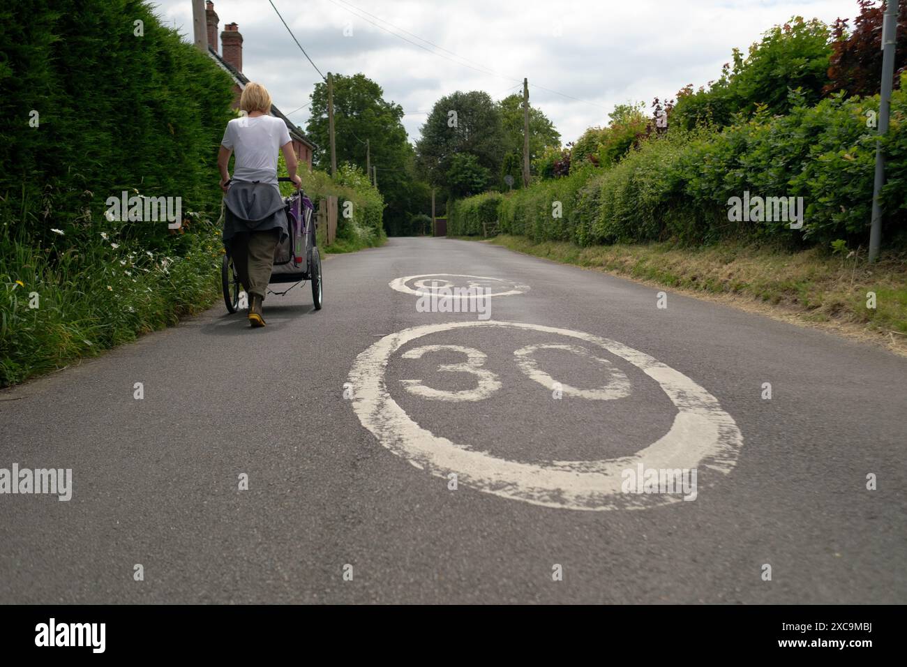 Une femme d'âge moyen marche le long d'une voie de campagne dans le hampshire Angleterre sur le côté gauche poussant un porte-chien à côté d'un panneau de route de 30 km/h. Banque D'Images