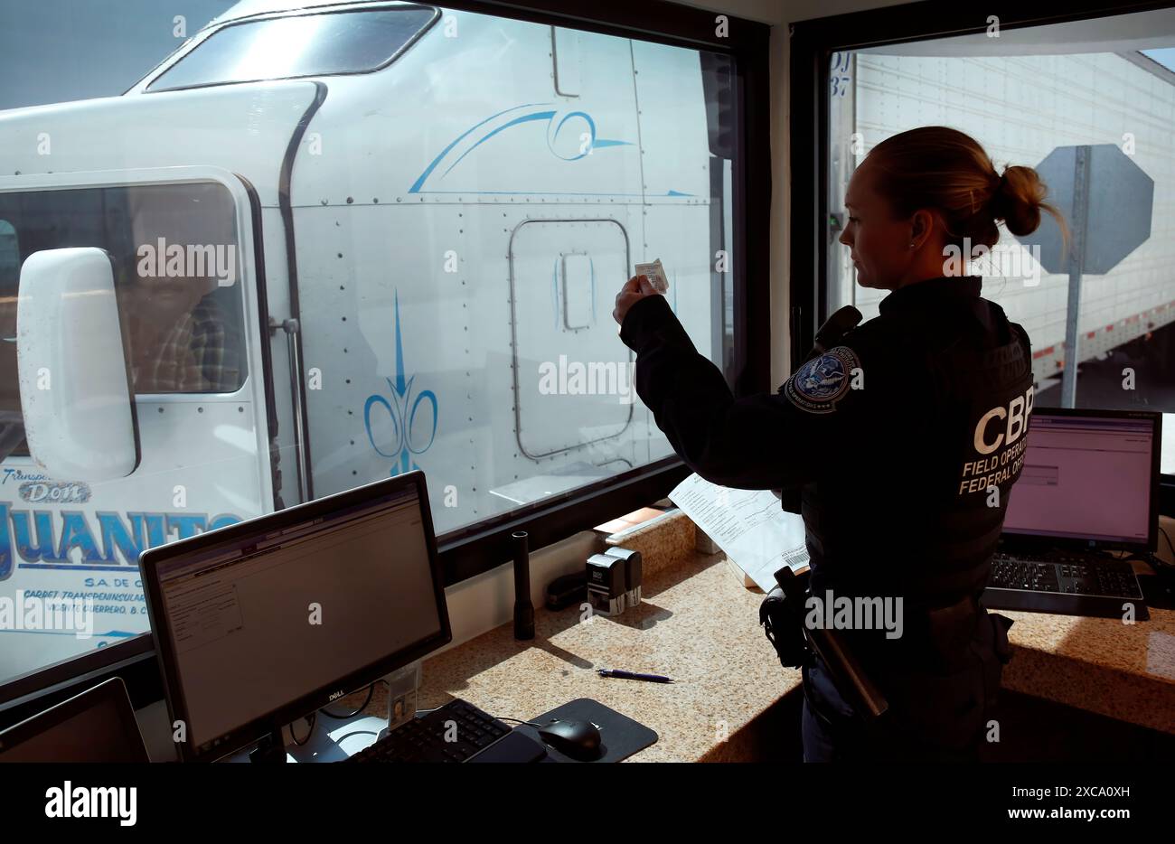 Un U.S. Customs and Border Protection préposé vérifie l'identification du conducteur du camion alors qu'il passe par le contrôle des États-Unis de la cargaison avant l'inspection à l'Otay Mesa, Californie, le port d'arrivée, le 22 juin 2016. Chaque jour, plusieurs centaines de camions alignés sur le côté mexicain de la frontière pour livrer les importations en attente en fin du processus de contrôle par les agents des douanes. Un nombre croissant de compagnies maritimes qui profitent de l'inspection du fret du CBP qui permet aux expéditeurs de confiance un moyen plus rapide et plus efficace de livrer des produits à des détaillants des États-Unis. Photo par Glenn Fawc CBP Banque D'Images