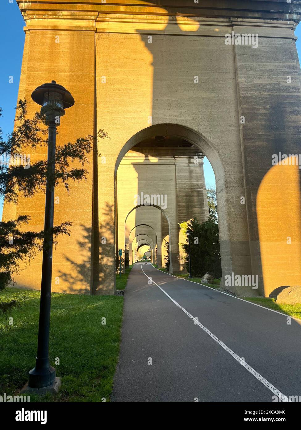 Une vue panoramique d'un sentier sous une série de grandes arches en pierre avec lumière du soleil projetant des ombres. Banque D'Images