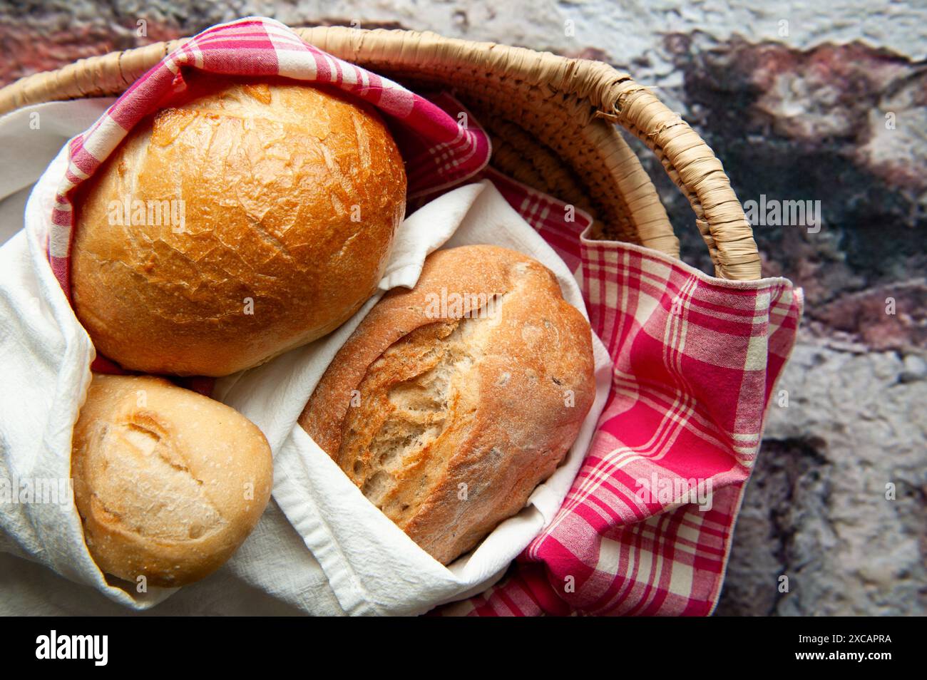 Une variété de différents pains artisanaux rustiques enveloppés dans une serviette à carreaux rouge et blanc dans un panier. Banque D'Images