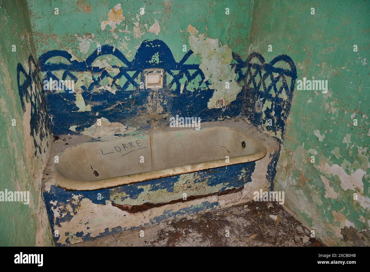 Salle de bains délabrée avec papier peint à motifs vert et bleu minable, vieille baignoire rouillée et murs décorés de couleurs décollées, palais du gouverneur italien, ruines Banque D'Images