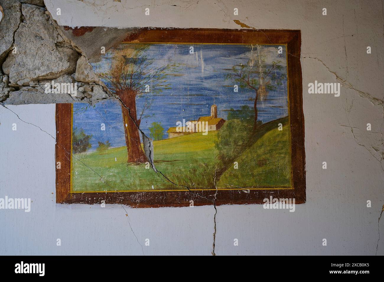 Sur un mur fissuré d'une maison abandonnée est une peinture d'une scène rurale avec un arbre, une église et des champs verts, lieu perdu, bunker de la seconde Guerre mondiale Banque D'Images