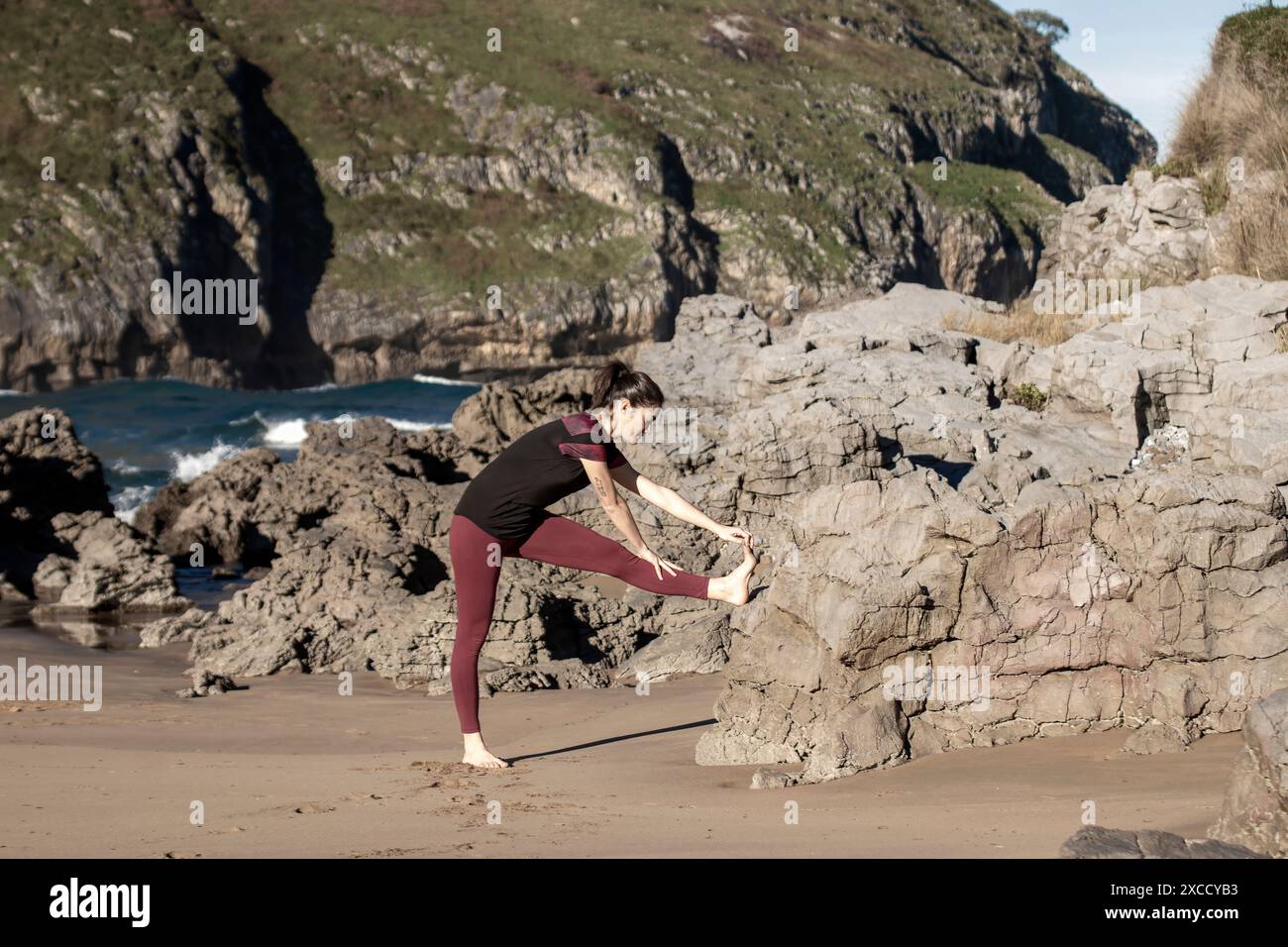 femme s'étirant sur une plage rocheuse en vêtements sportifs. Concept de fitness et d'exercice en plein air Banque D'Images