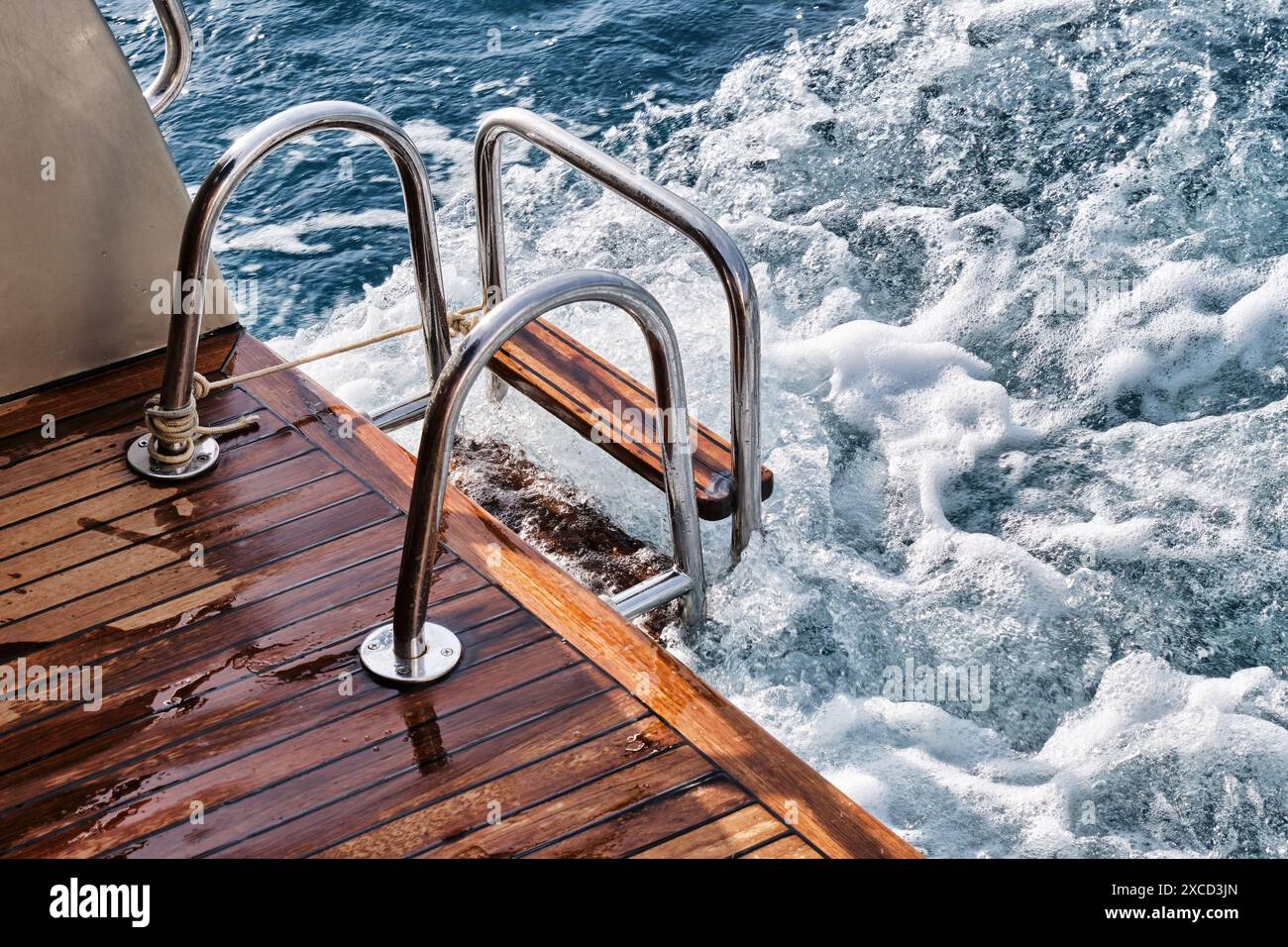Pont arrière en bois de teck et échelle métallique d'un yacht à moteur, vagues et éclaboussures de mer et mousse. Banque D'Images