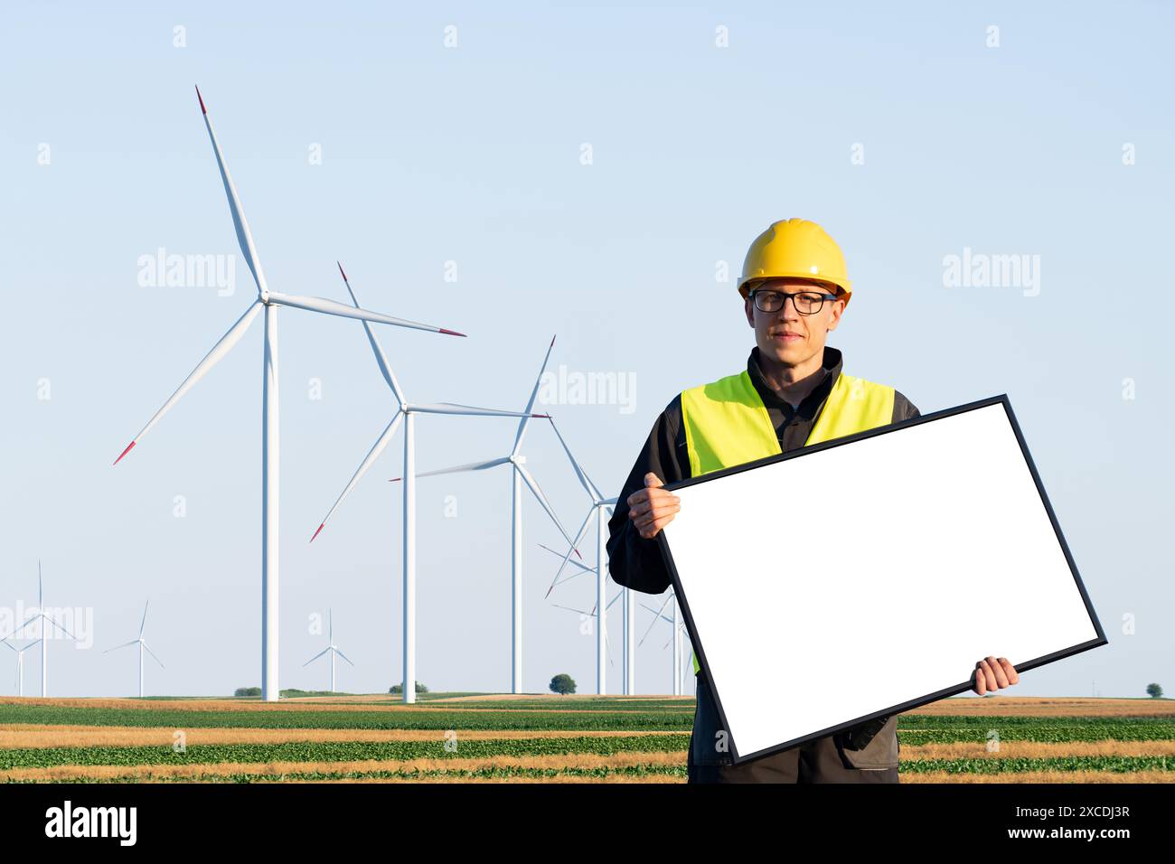 Travailleur en casque avec un tableau blanc vierge sur un champ d'éoliennes. Espace vide, vous pouvez ajouter votre texte ici. Banque D'Images