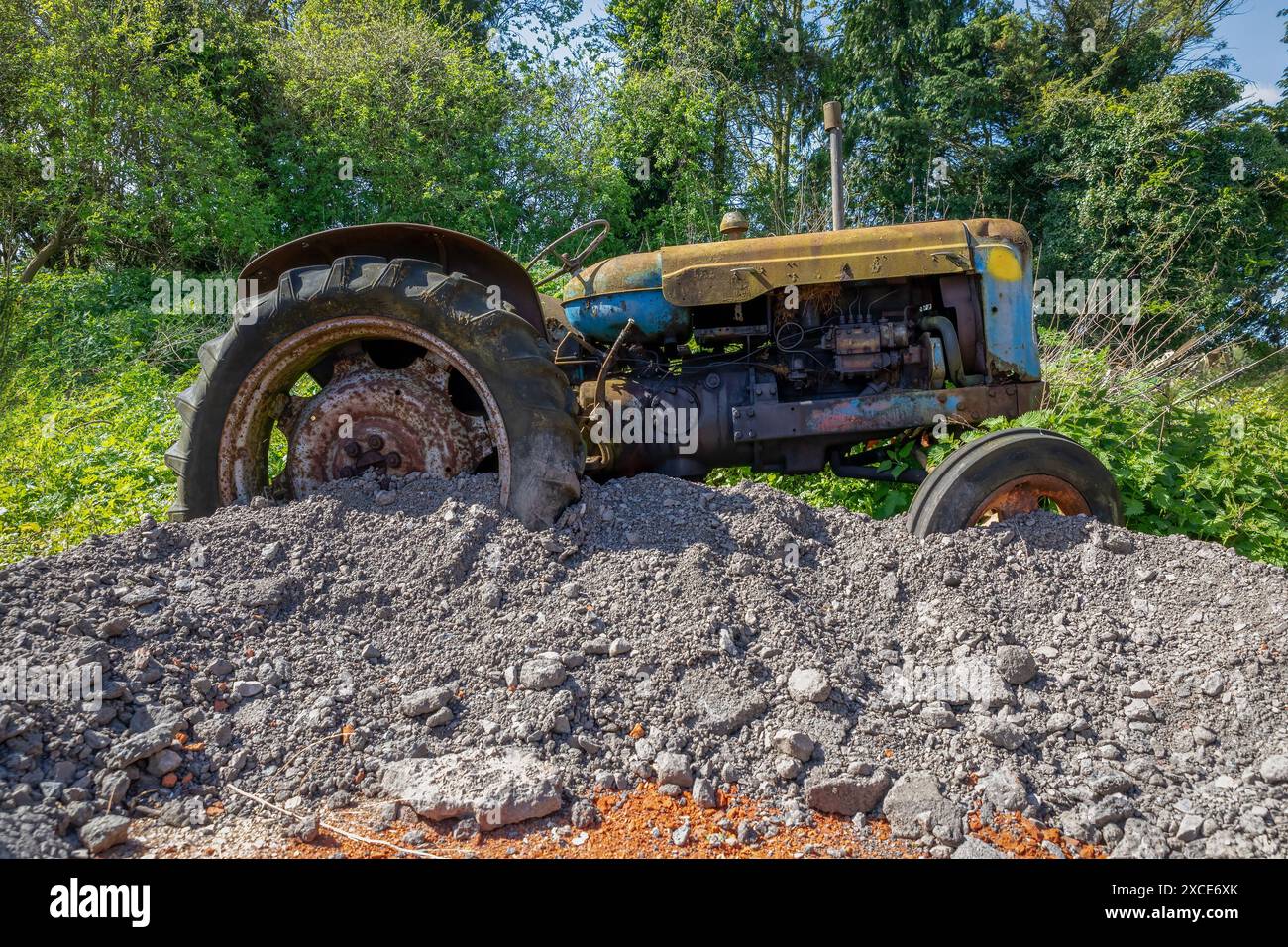 Vue latérale rapprochée d'un tracteur agricole abandonné. Dans un état de délabrement, il est garé sur un noyau dur dans un champ. Banque D'Images