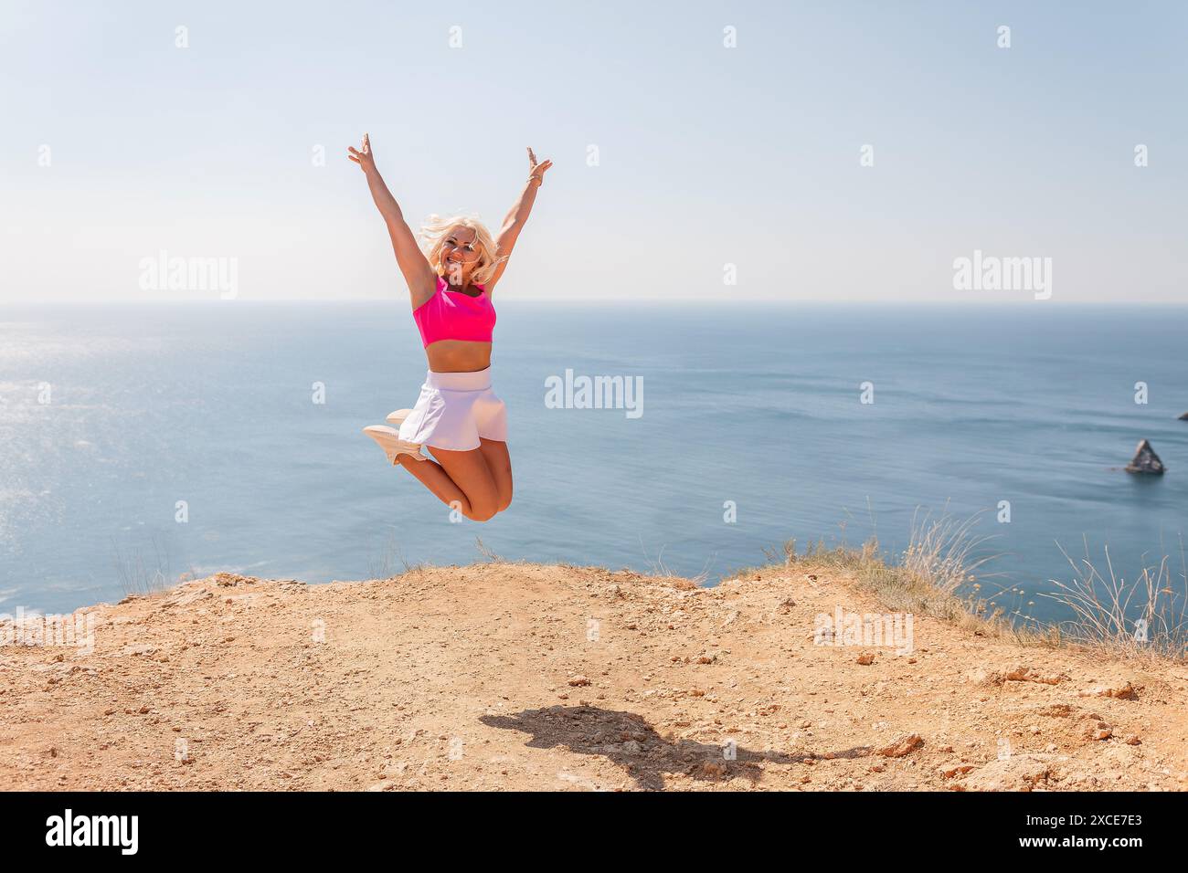 Une femme saute dans les airs sur une plage avec l'océan en arrière-plan Banque D'Images