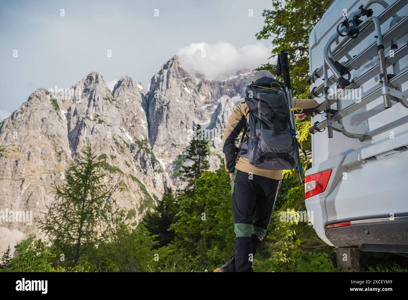 Un randonneur se tient près d'un camping-car, se préparant pour un trek dans les montagnes. Ils portent un sac à dos et portent des bâtons de randonnée, face à une toile de fond de Banque D'Images