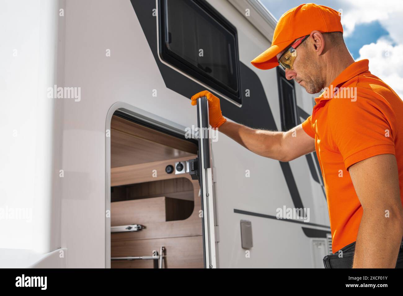 Le technicien de camping-car ouvre le compartiment de rangement d'une fourgonnette blanche. Le compartiment est situé sur le côté de la fourgonnette et est partiellement ouvert, révélateur Banque D'Images