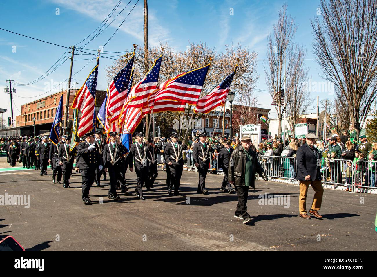 Lindenhurst, New York, États-Unis, le 30 mars 2024 - des marcheurs en uniforme portant des drapeaux américains marchent fièrement dans Une rue ensoleillée pendant Un défilé, avec Une foule animée de spectateurs alignés sur les côtés, célébrant Un événement patriotique dans un cadre urbain. Banque D'Images